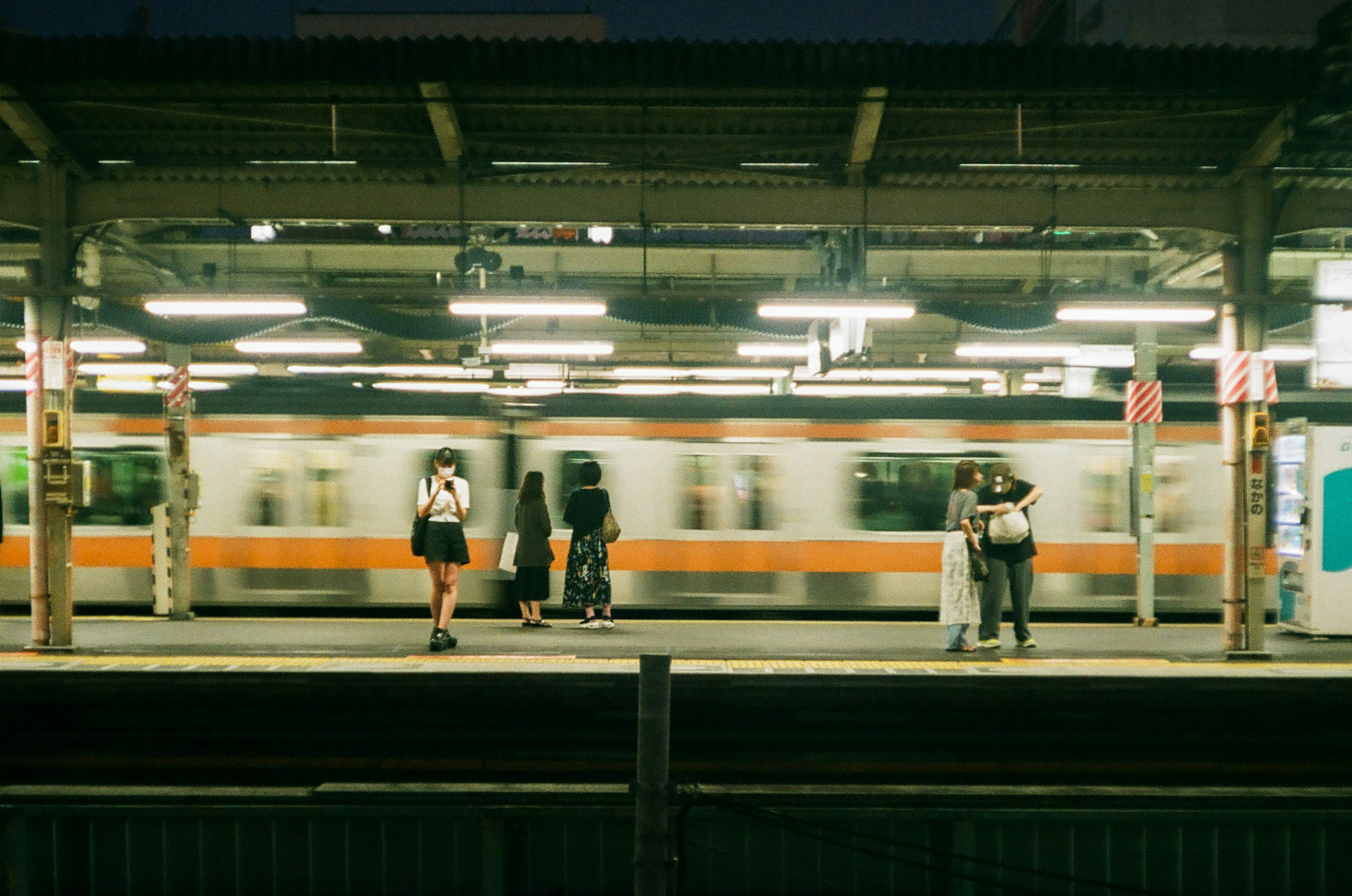 駅のプラットフォームで電車が通過するシーン 人々が待っている 照明が明るい