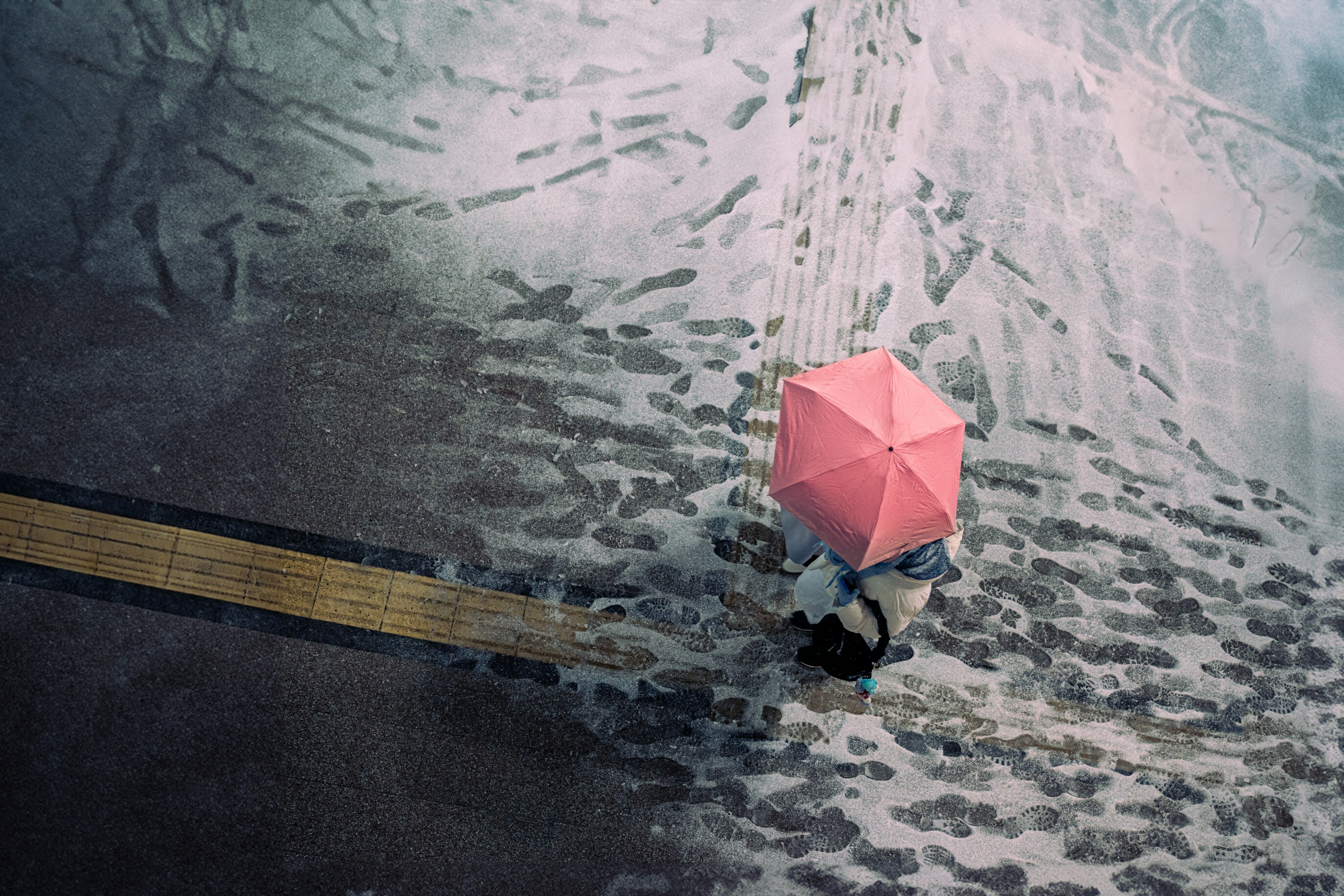 A person walking with a pink umbrella over a wet pavement