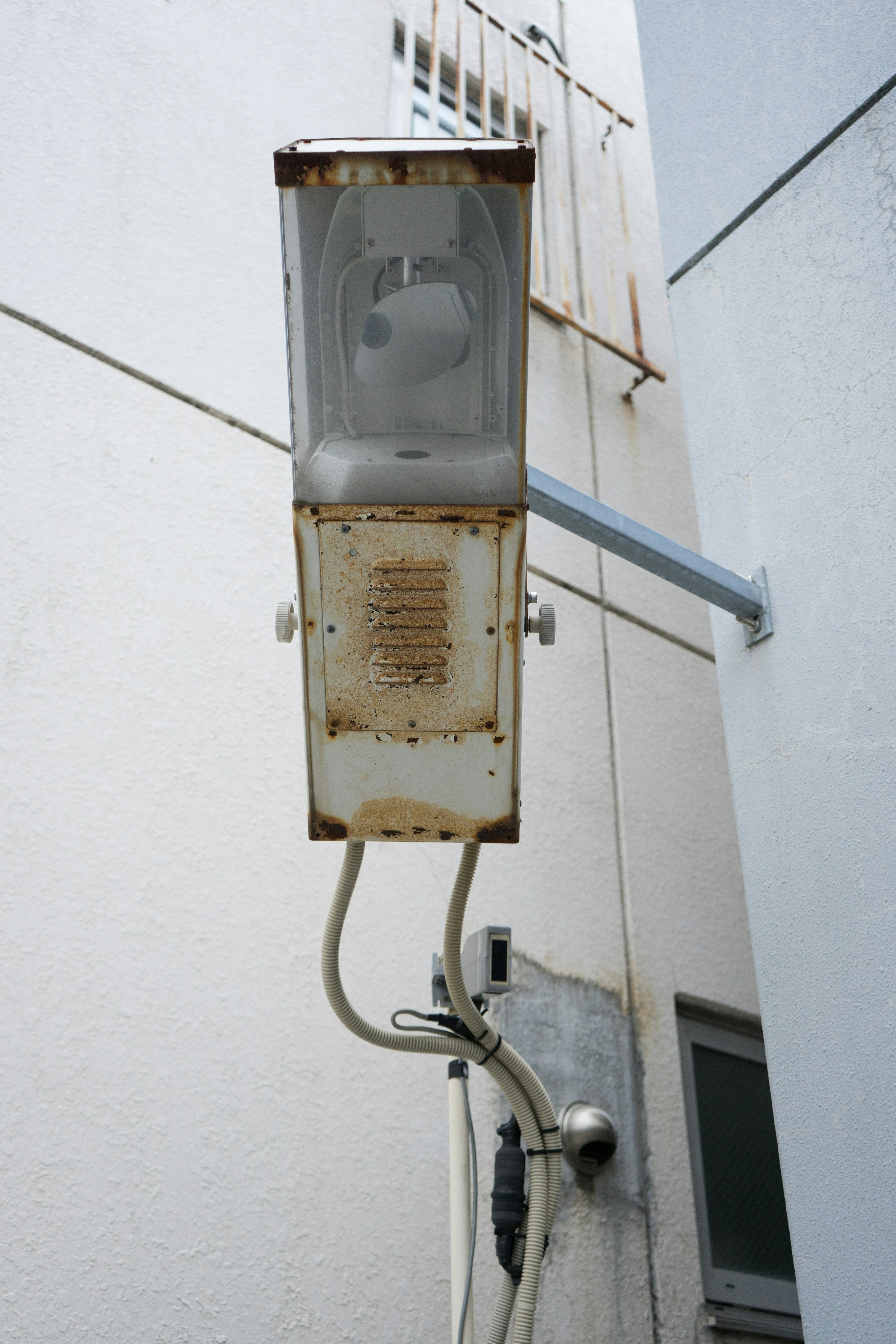 Eine alte Straßenlaterne an einer Wand montiert, die den Kontrast zwischen rostigem Metall und einer weißen Wand zeigt