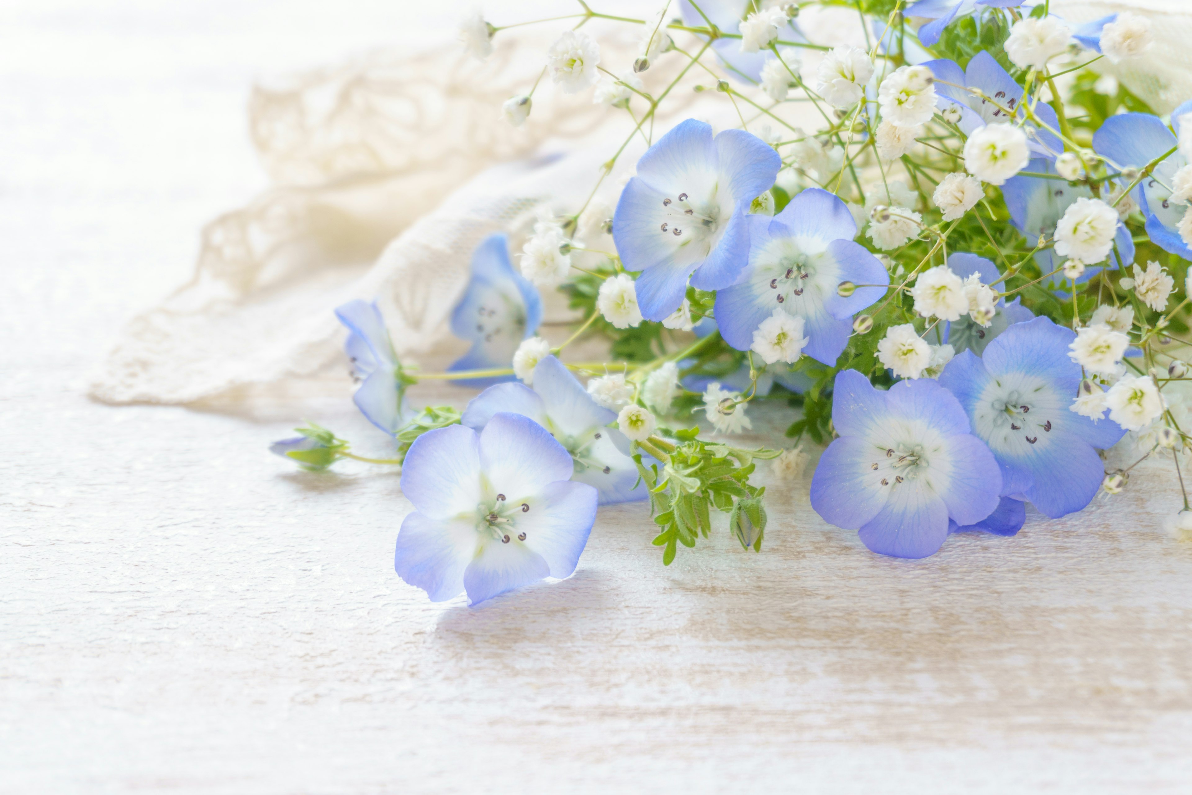 Un mazzo di fiori blu e piccoli fiori bianchi su un tavolo in legno bianco