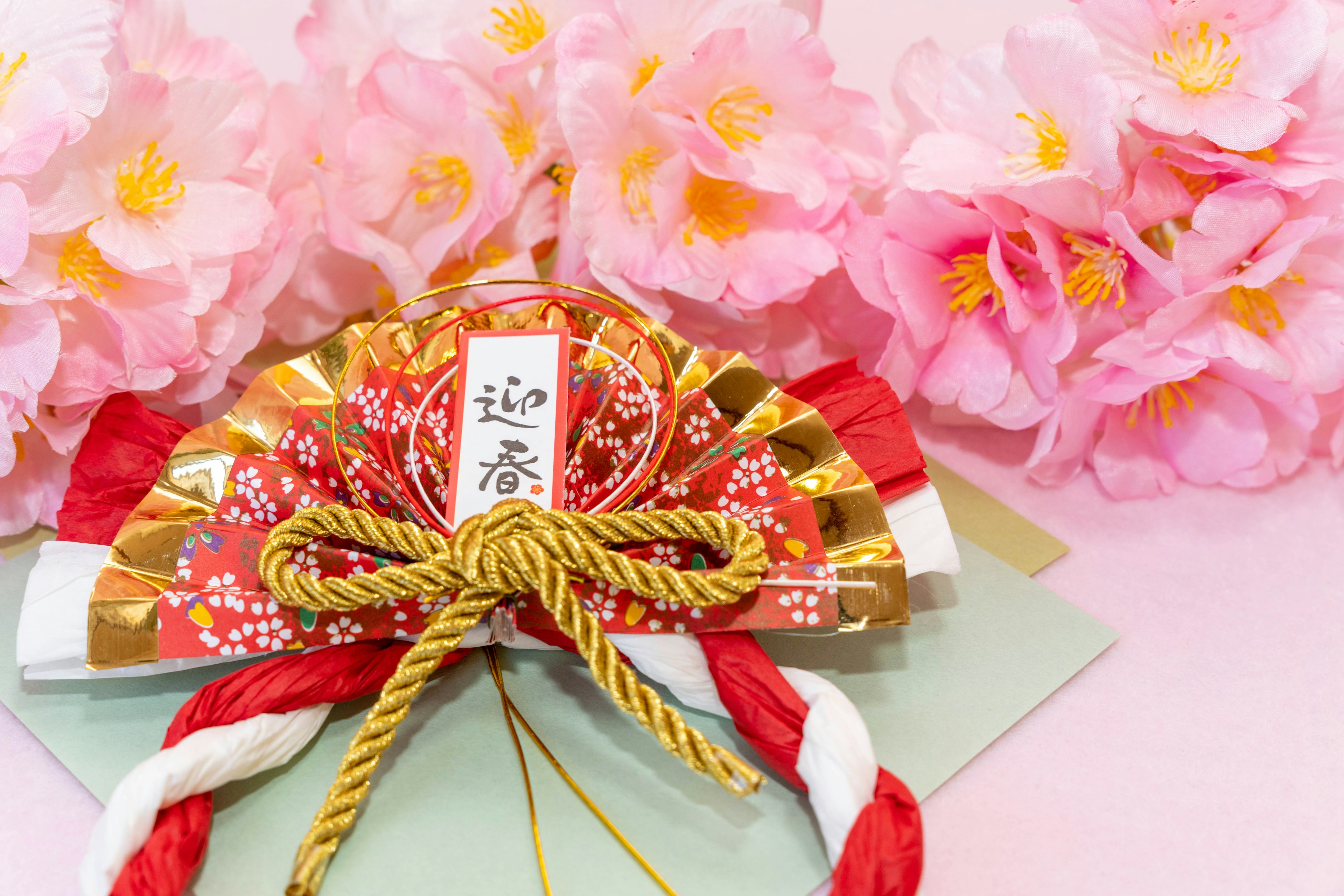 A decorative Japanese envelope with a red and gold ribbon and cherry blossoms in the background