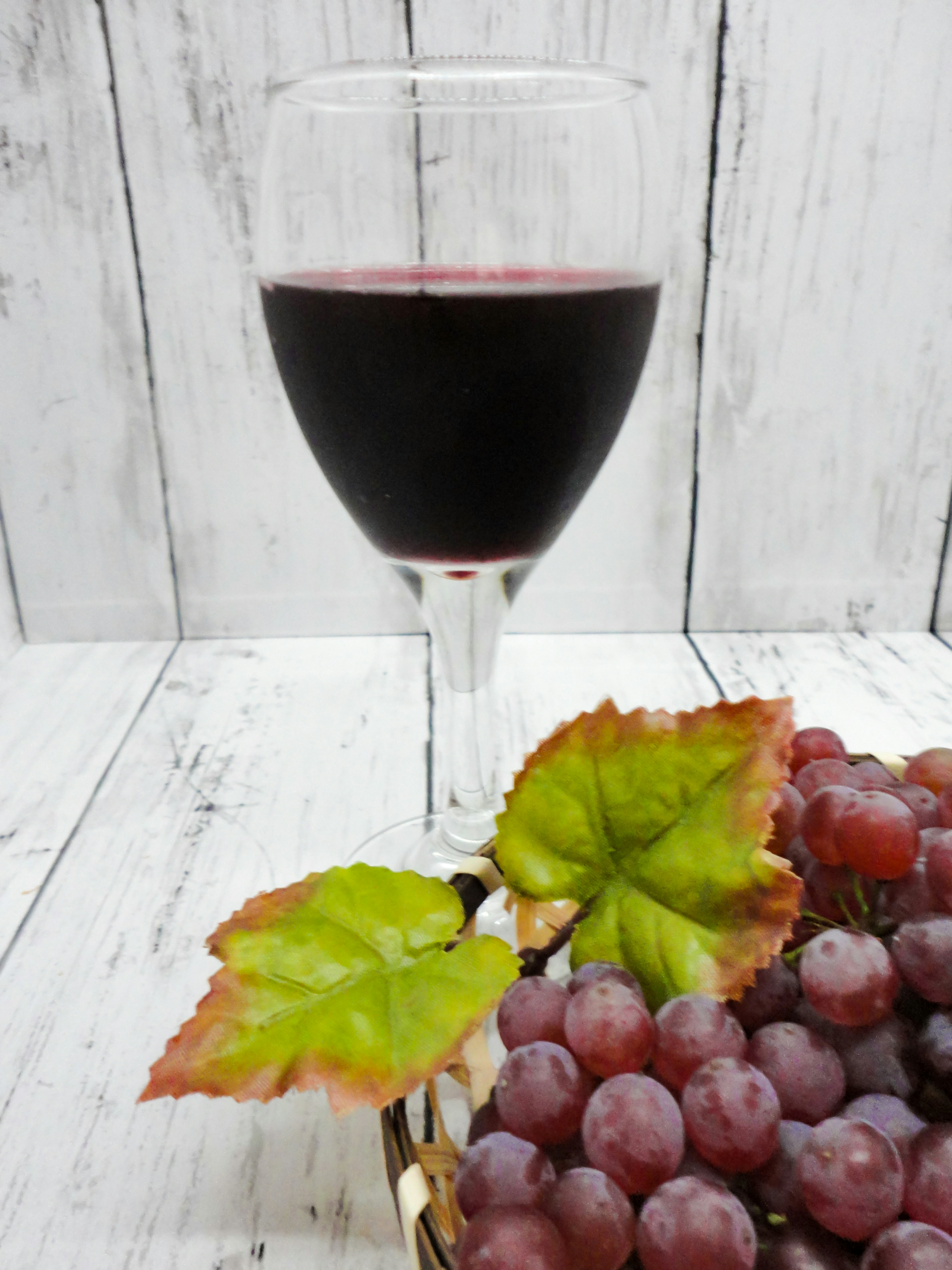 A glass of red wine beside a bunch of grapes and green leaves