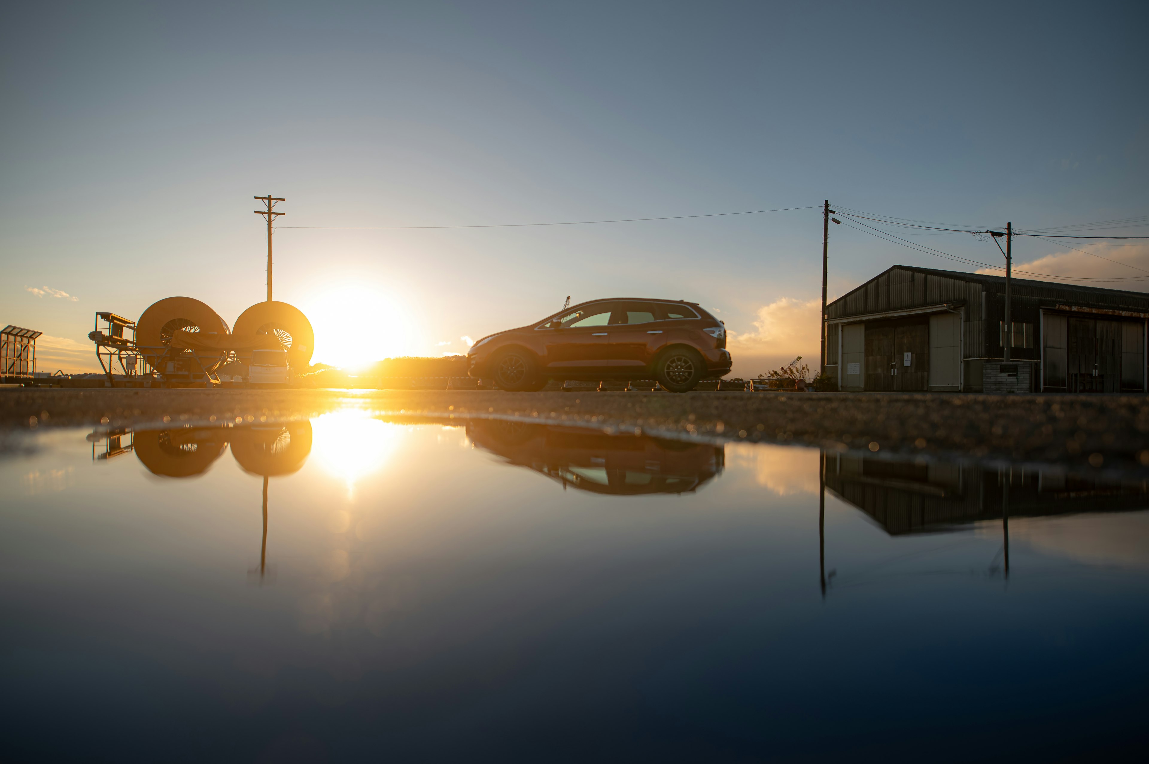 水面に映る夕日と車の景色 近くに小屋とタイヤが並ぶ