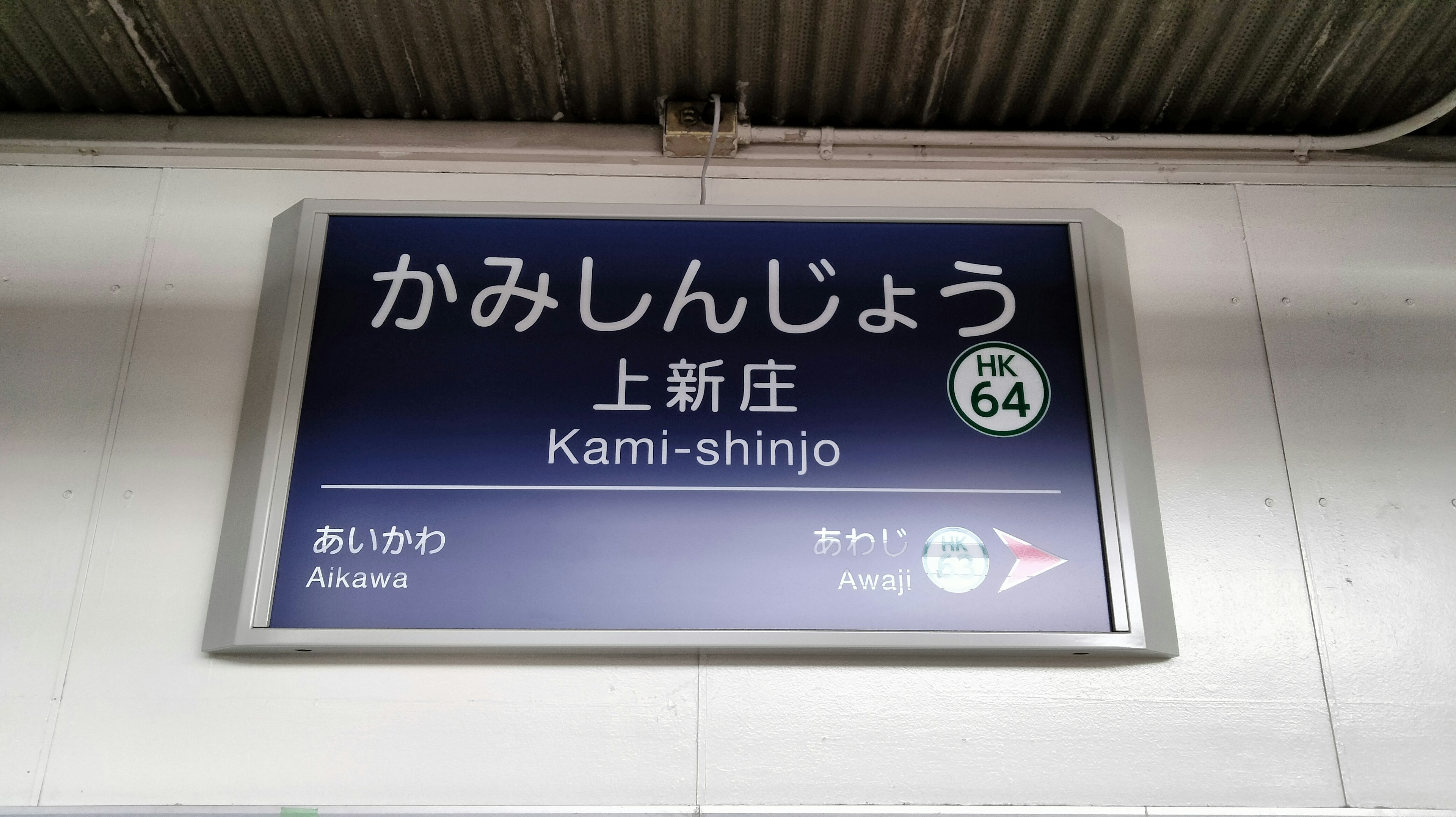 Cartel de la estación Kami-shinjo que muestra el nombre en japonés e inglés