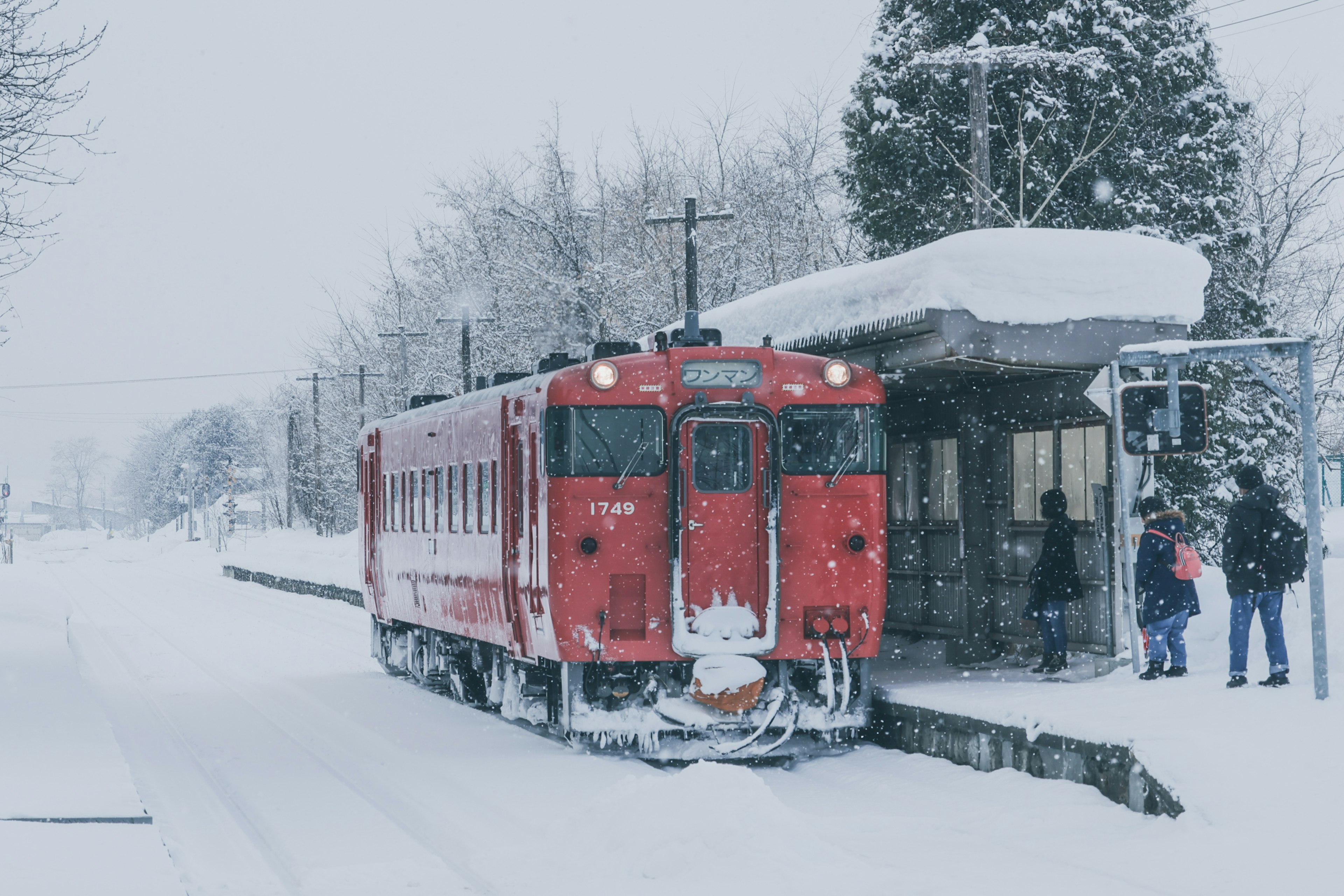 รถไฟแดงที่สถานีที่มีหิมะปกคลุมและผู้โดยสารรออยู่