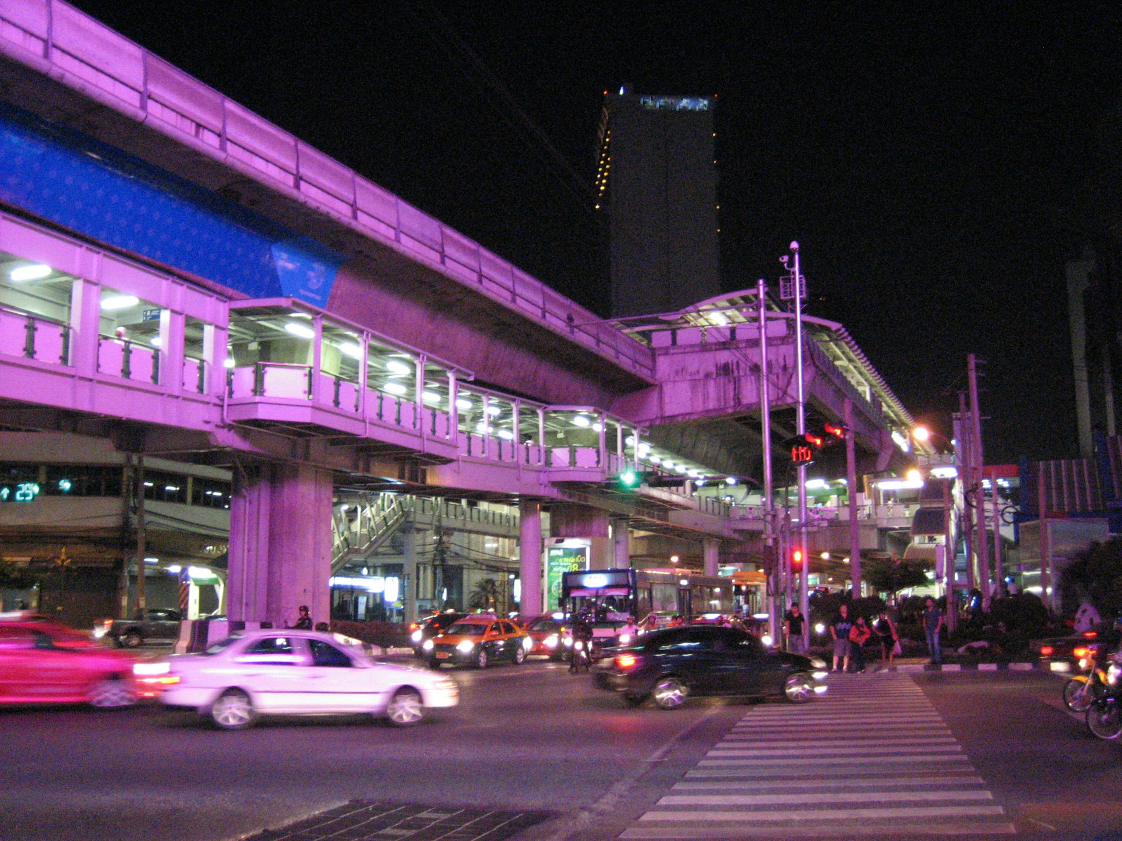 Urban night scene featuring elevated train and busy intersection with striking pink lighting