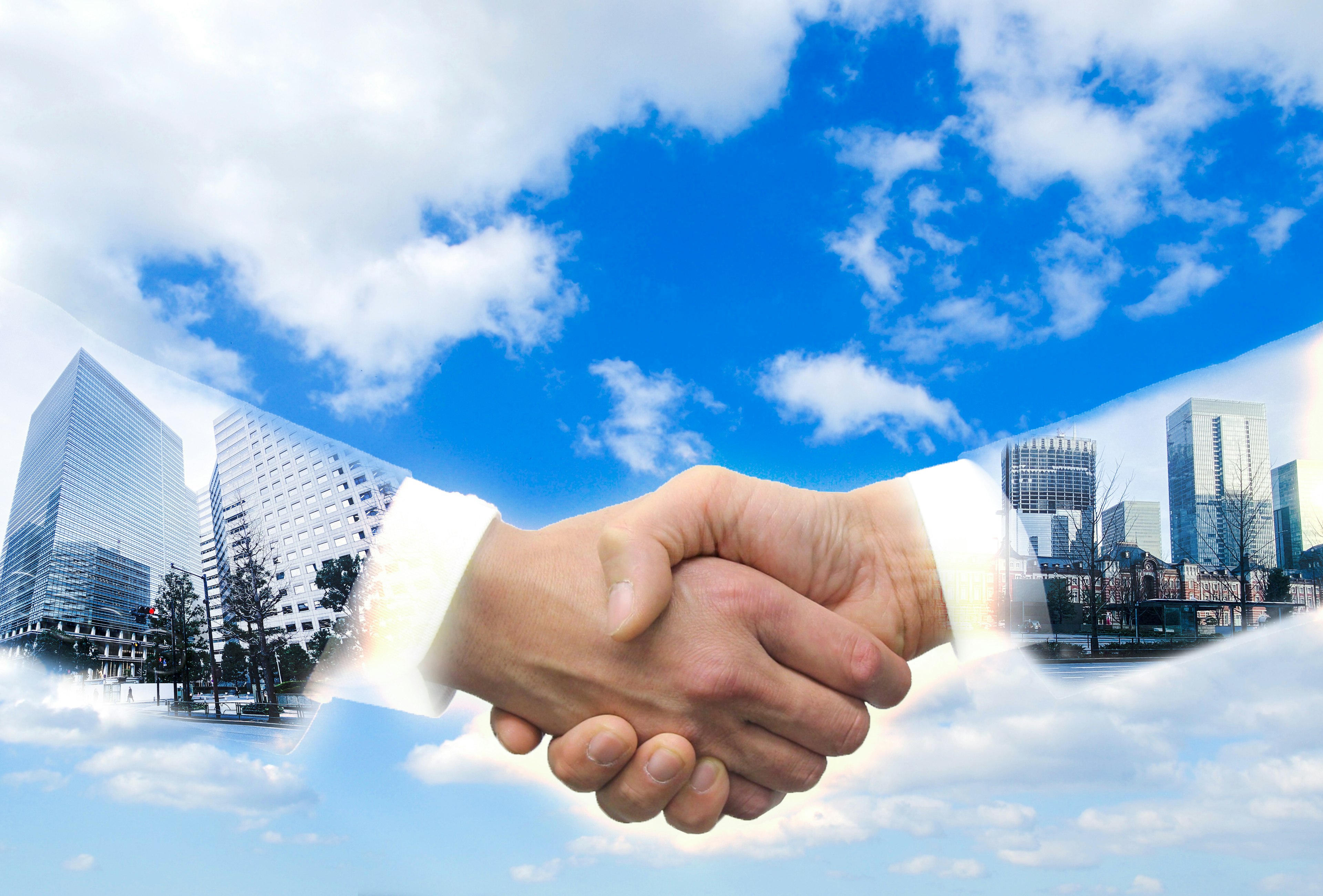 Image of a handshake under a blue sky with silhouettes of buildings overlapping