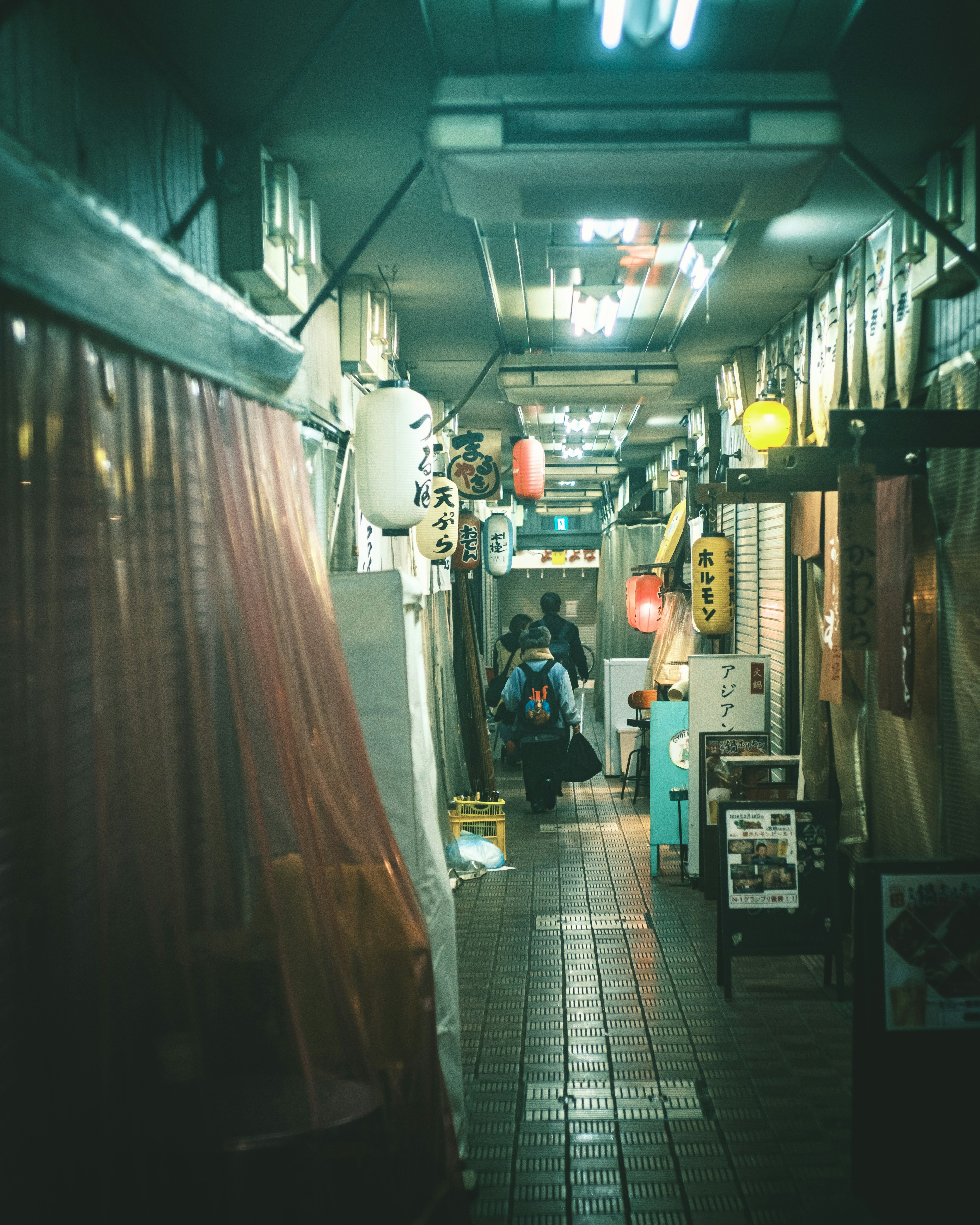 Narrow corridor lined with restaurant entrances and illuminated lanterns