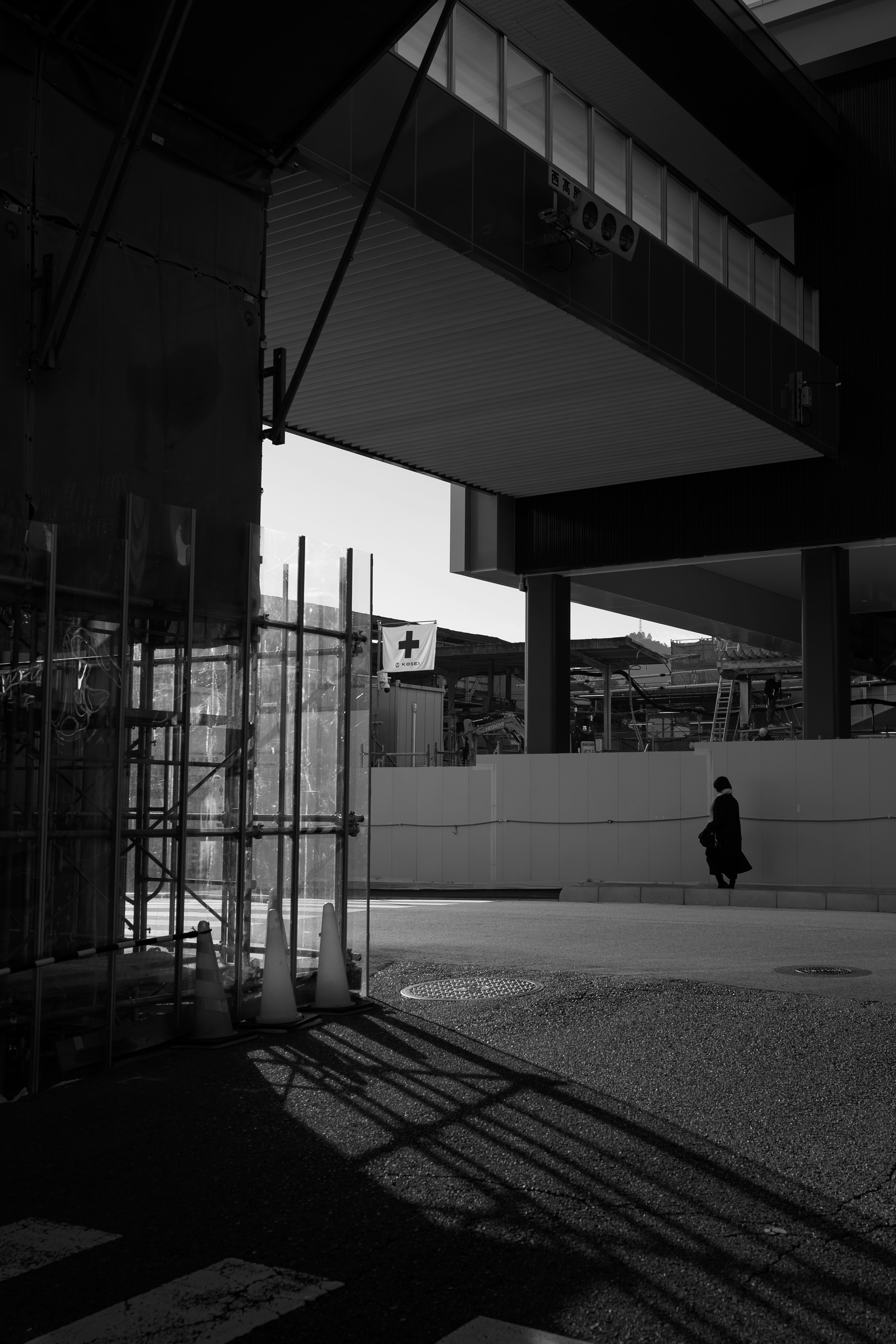 Escena urbana en blanco y negro con sombras de edificios y una figura solitaria