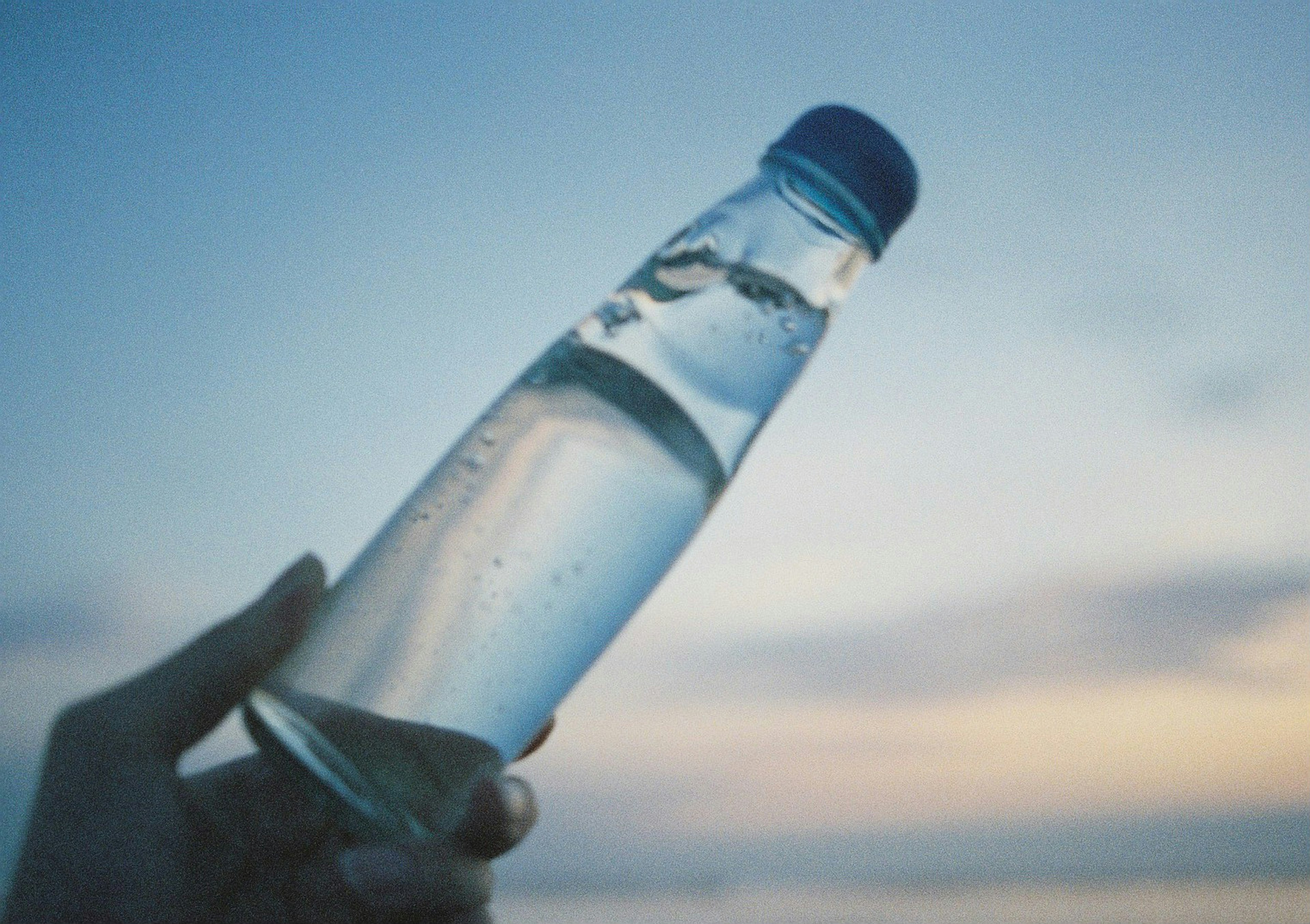 Hand holding a water bottle against a blue sky background