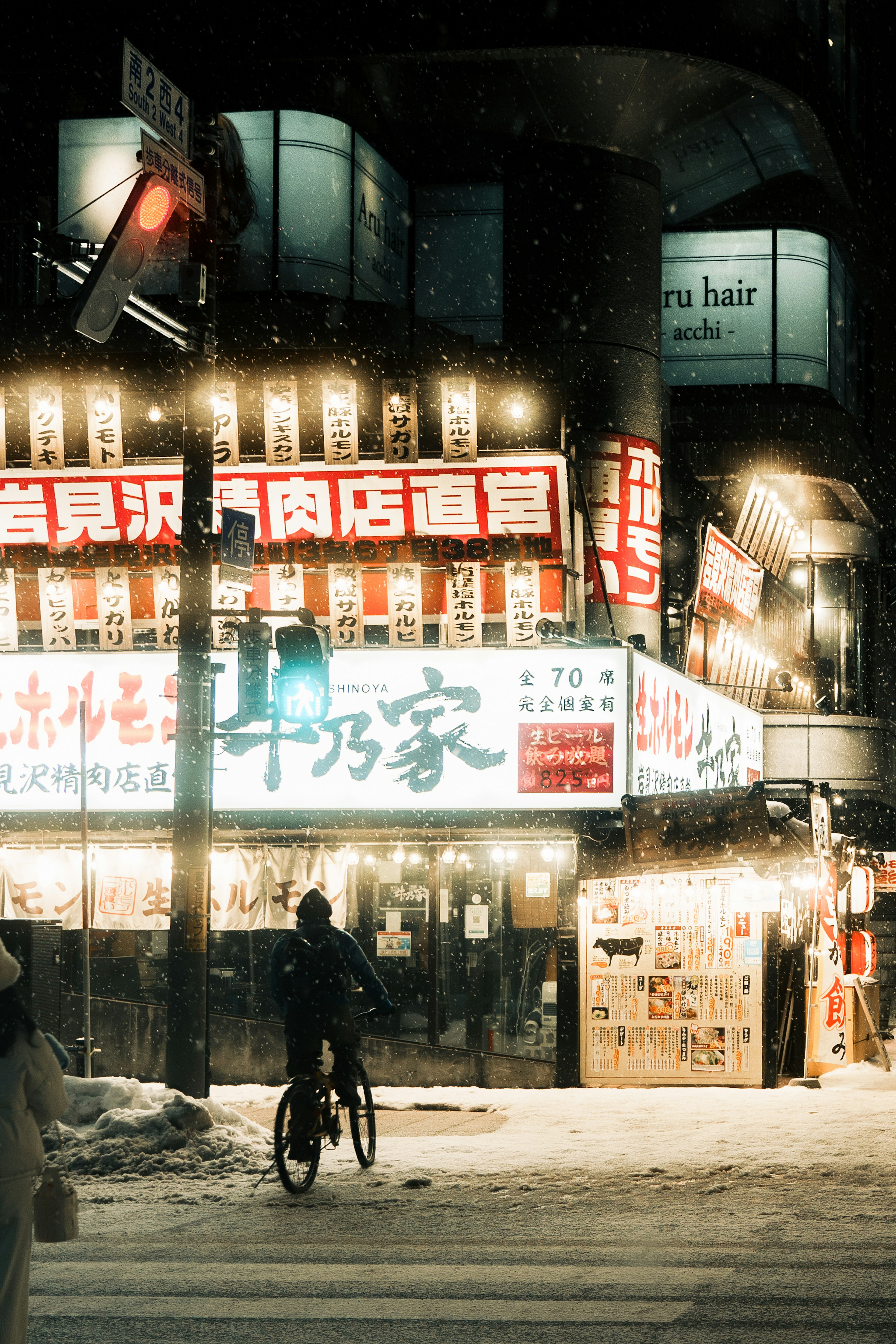 Person riding a bicycle in the snow with bright signs in a nighttime city