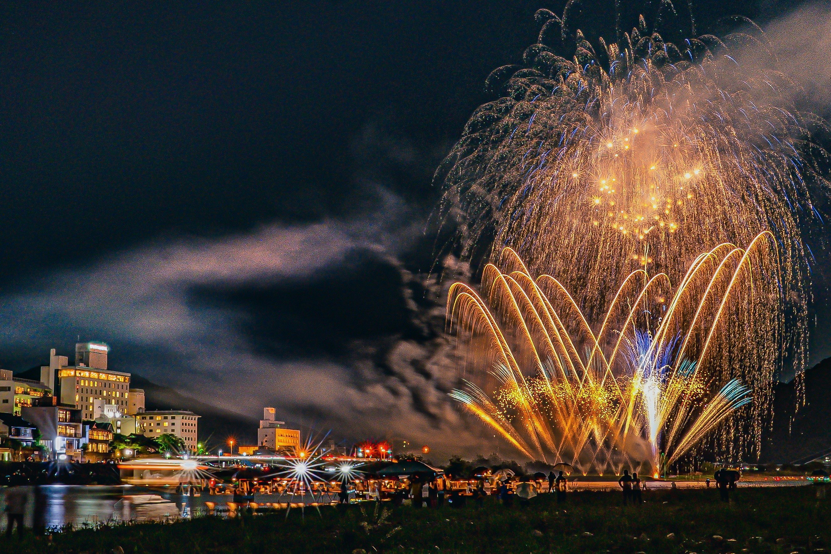 Spectacle de feux d'artifice colorés au-dessus d'une rivière avec des bâtiments illuminés la nuit