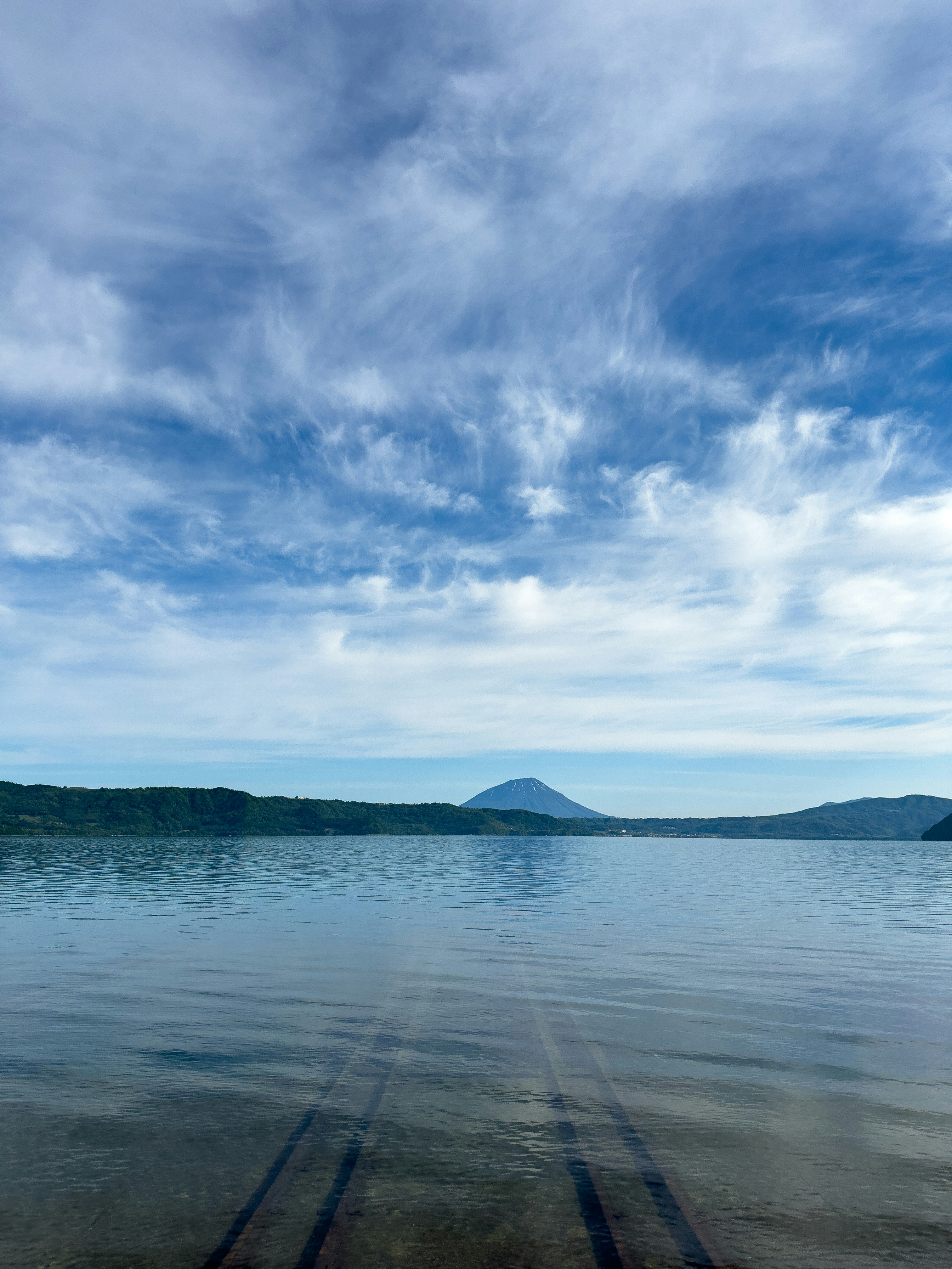 Tranquil lake reflecting distant mountains under a blue sky