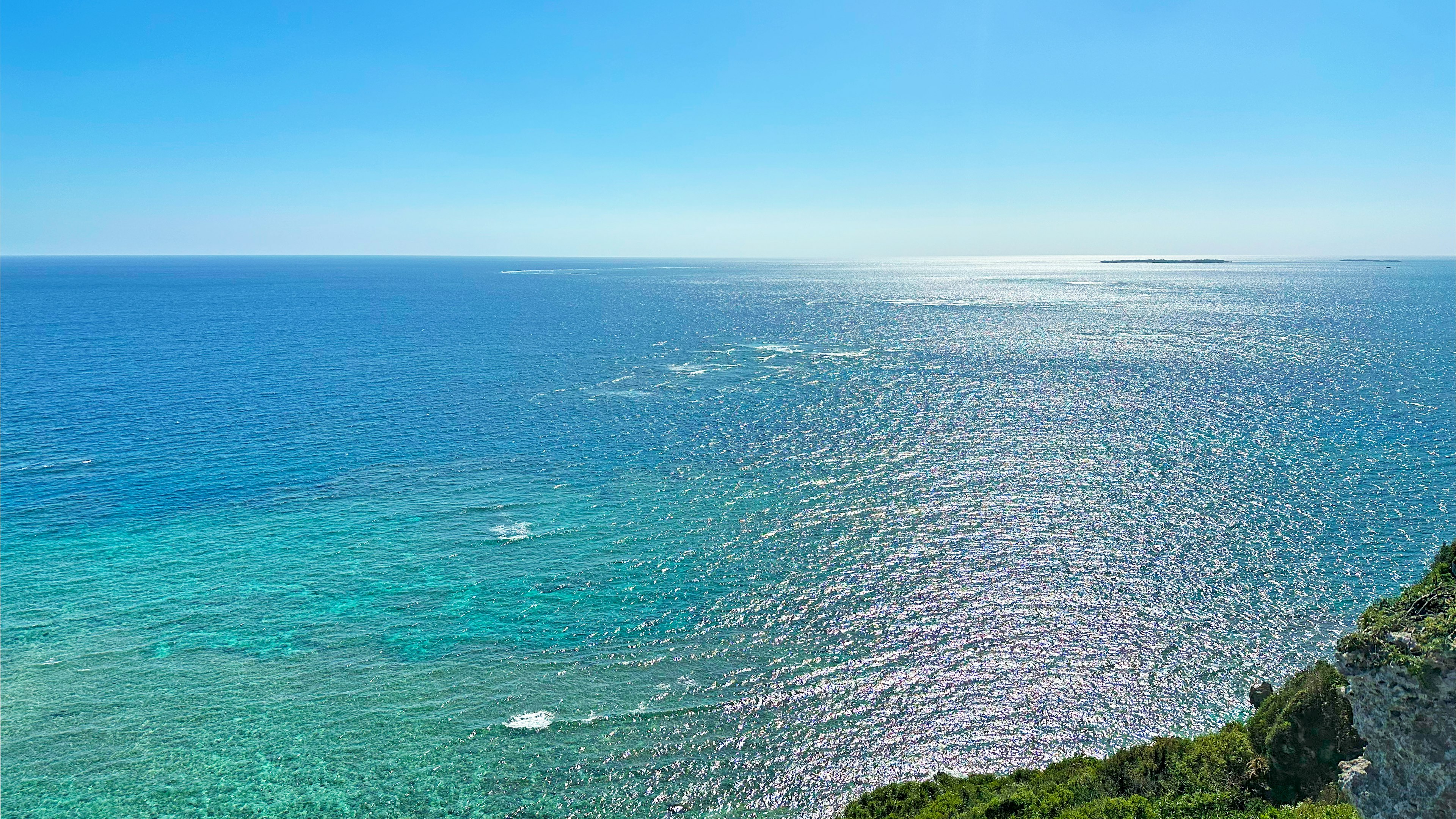 Vasto oceano blu e cielo con scogliere verdi in primo piano