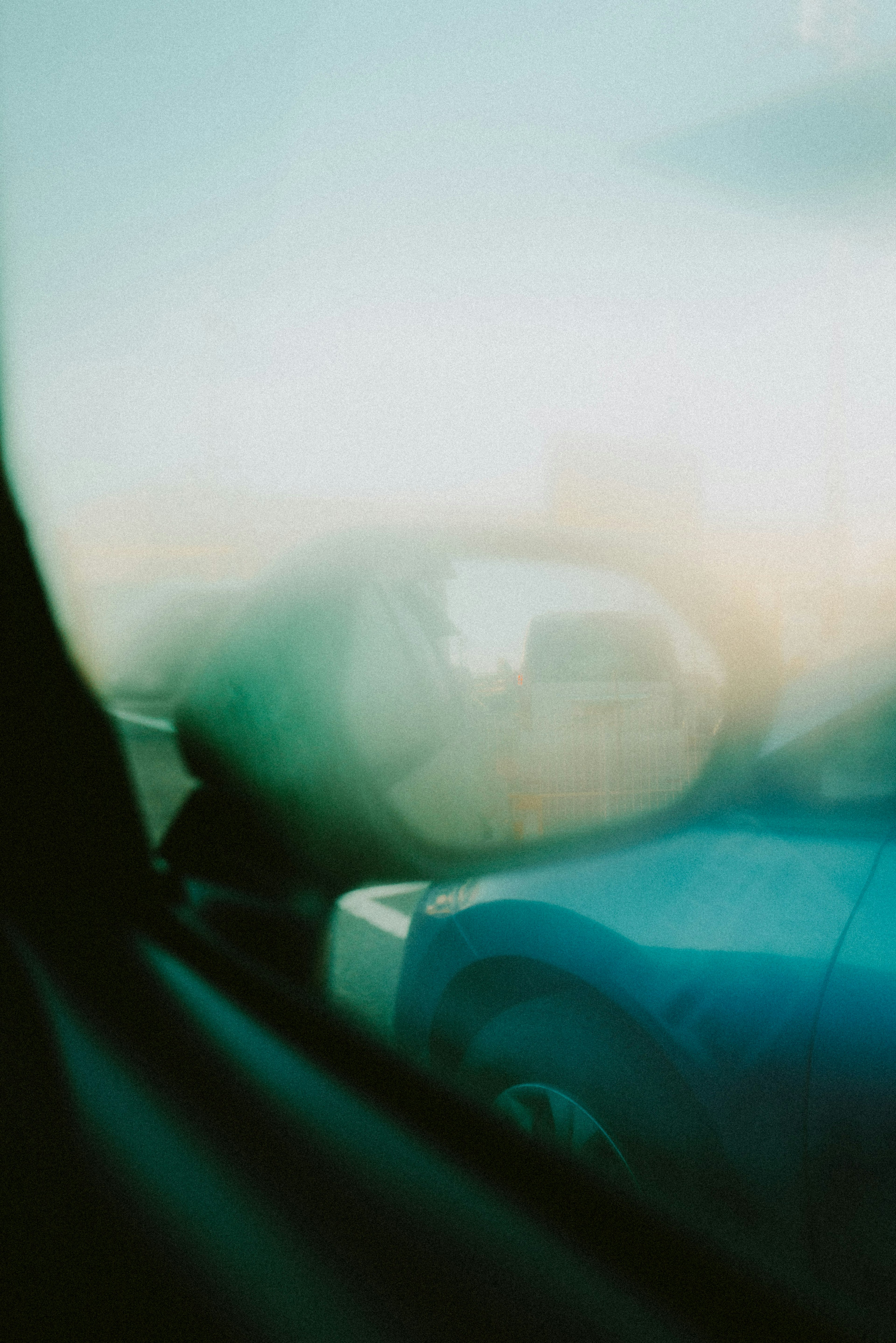 Verschommene Sicht auf ein blaues Auto durch ein beschlagenes Fenster mit weichem Hintergrund