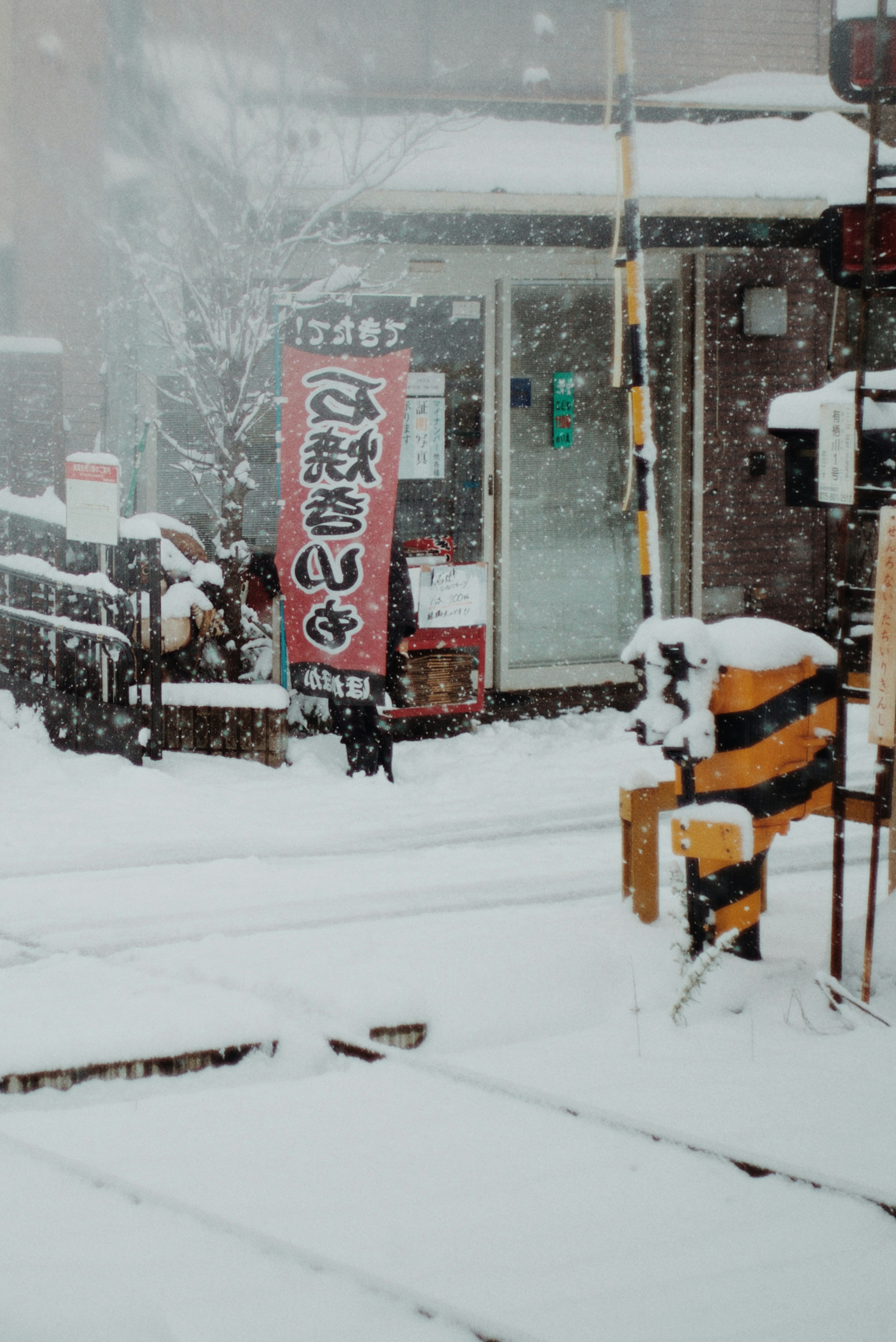 A snowy scene featuring a train station sign and crossing barrier