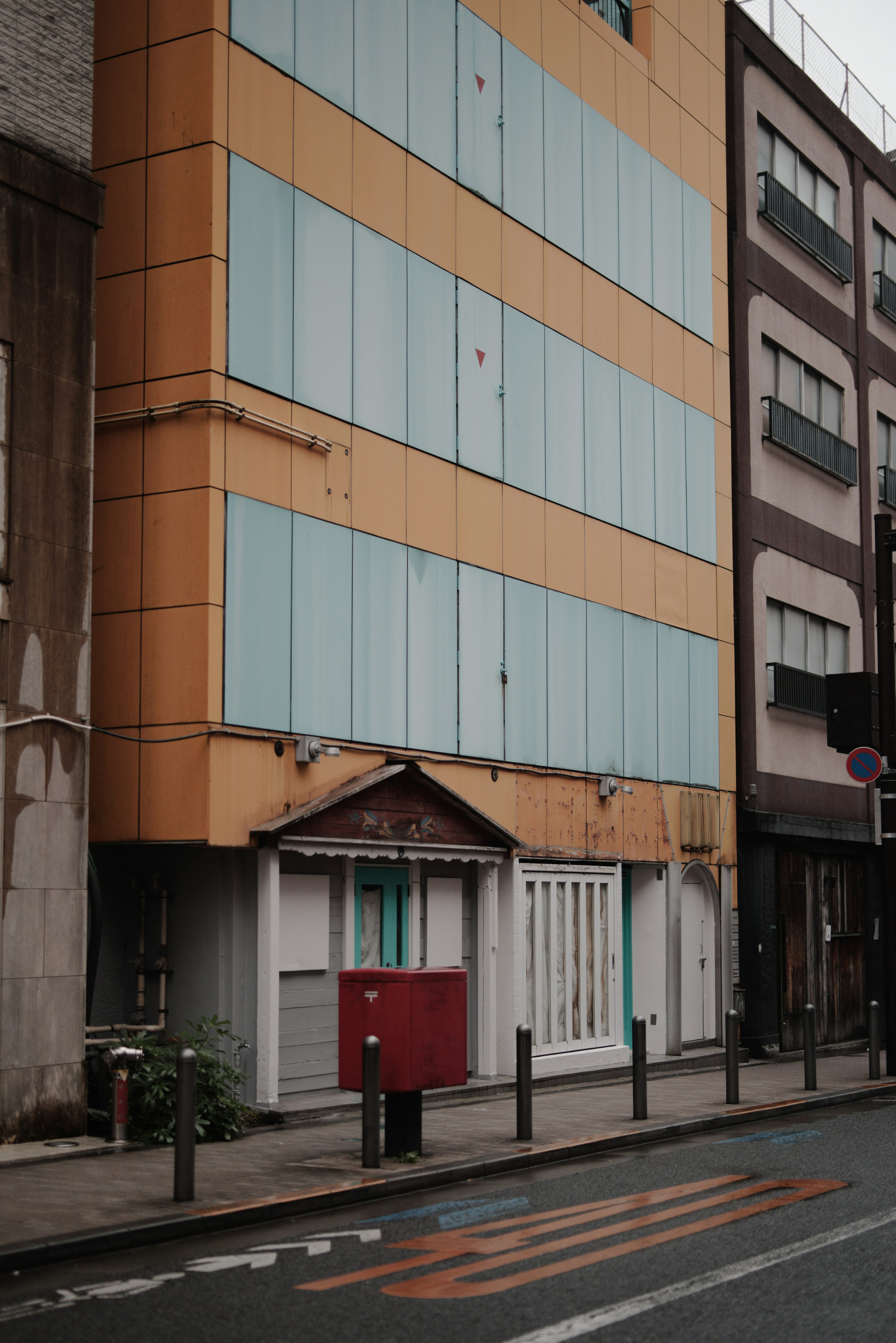 Street view featuring a unique building with blue shutters and a small red mailbox