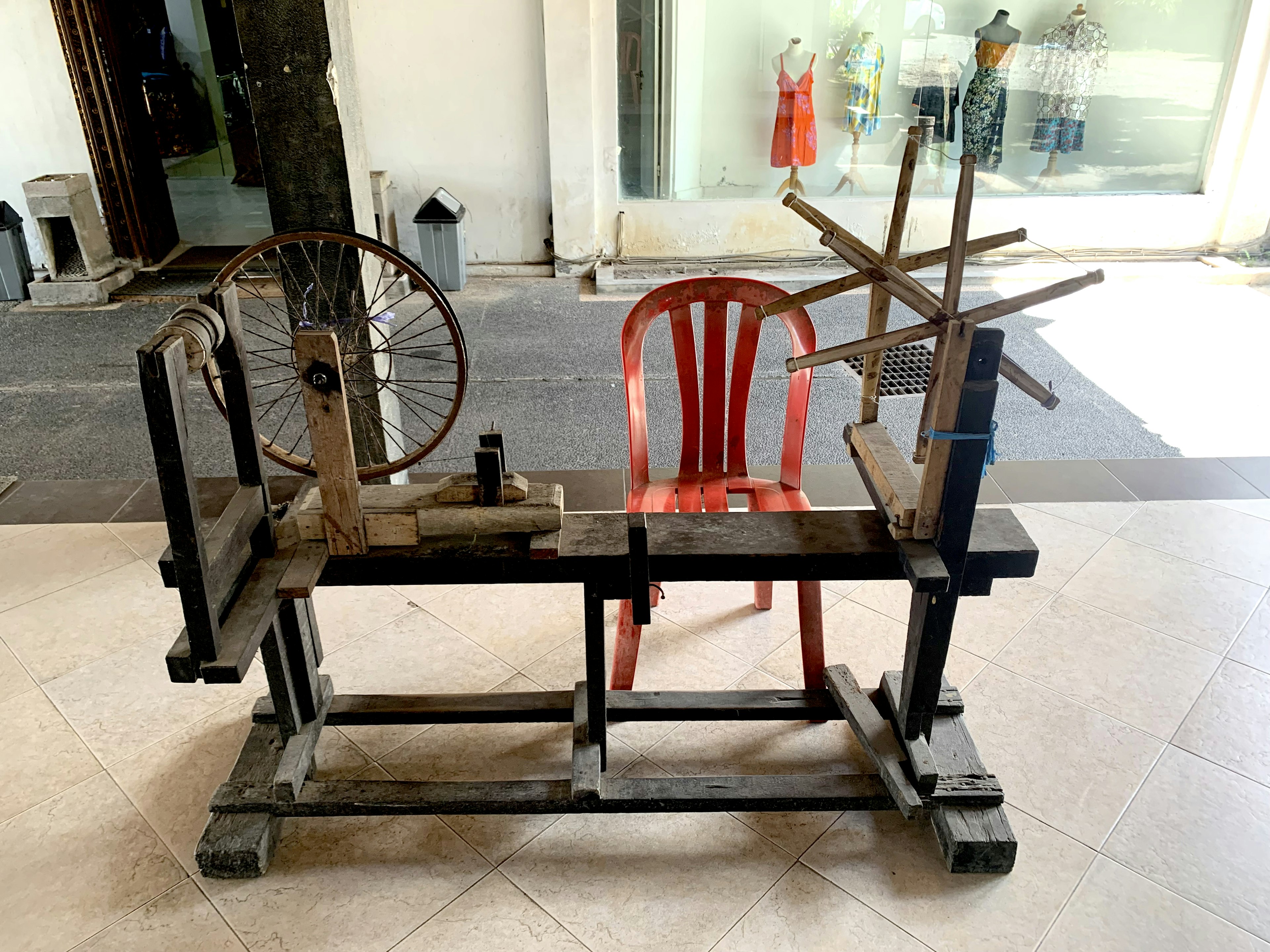 Traditional wooden spinning wheel with a red chair in a craft setting