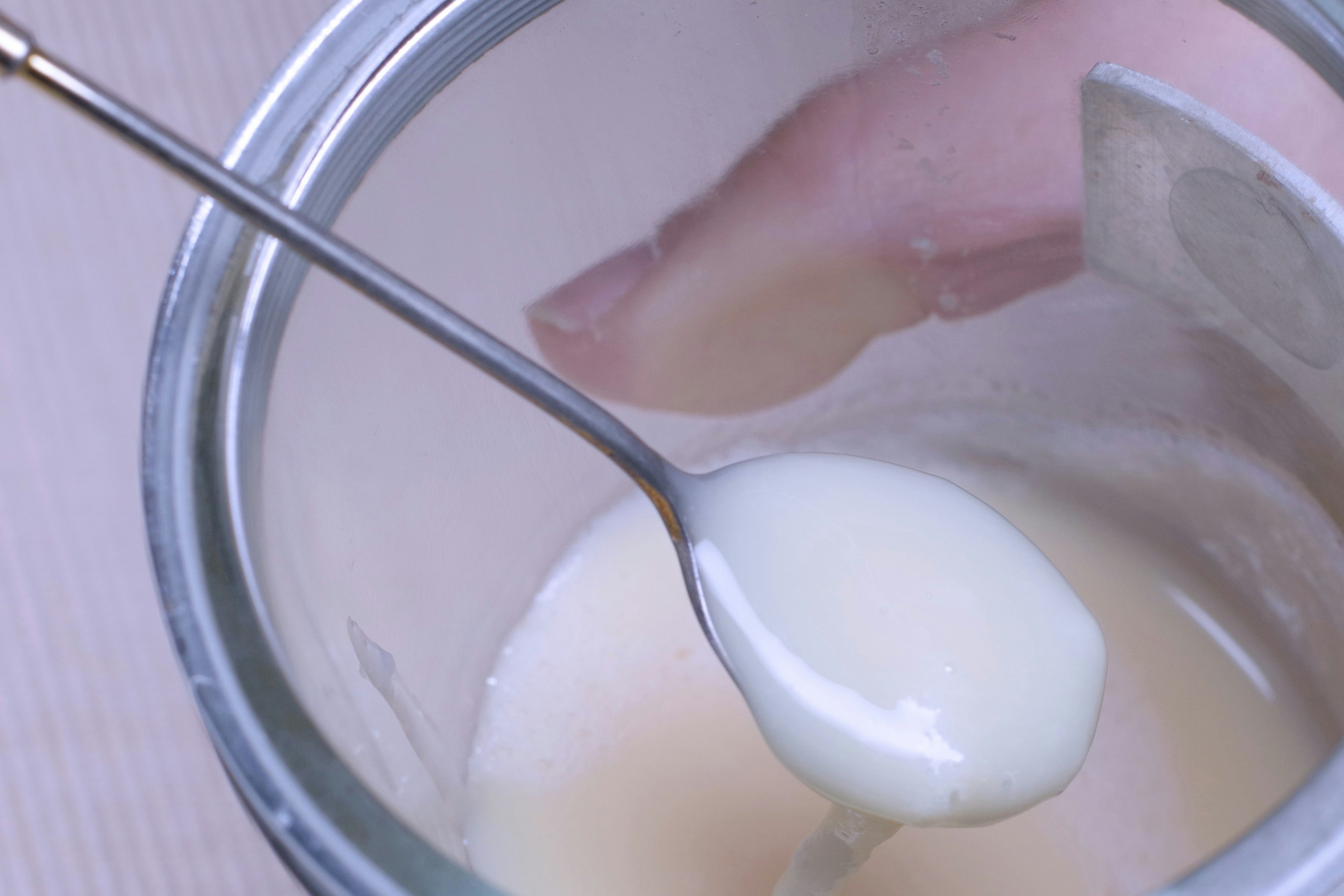 Un cucchiaio di liquido cremoso con una mano sullo sfondo