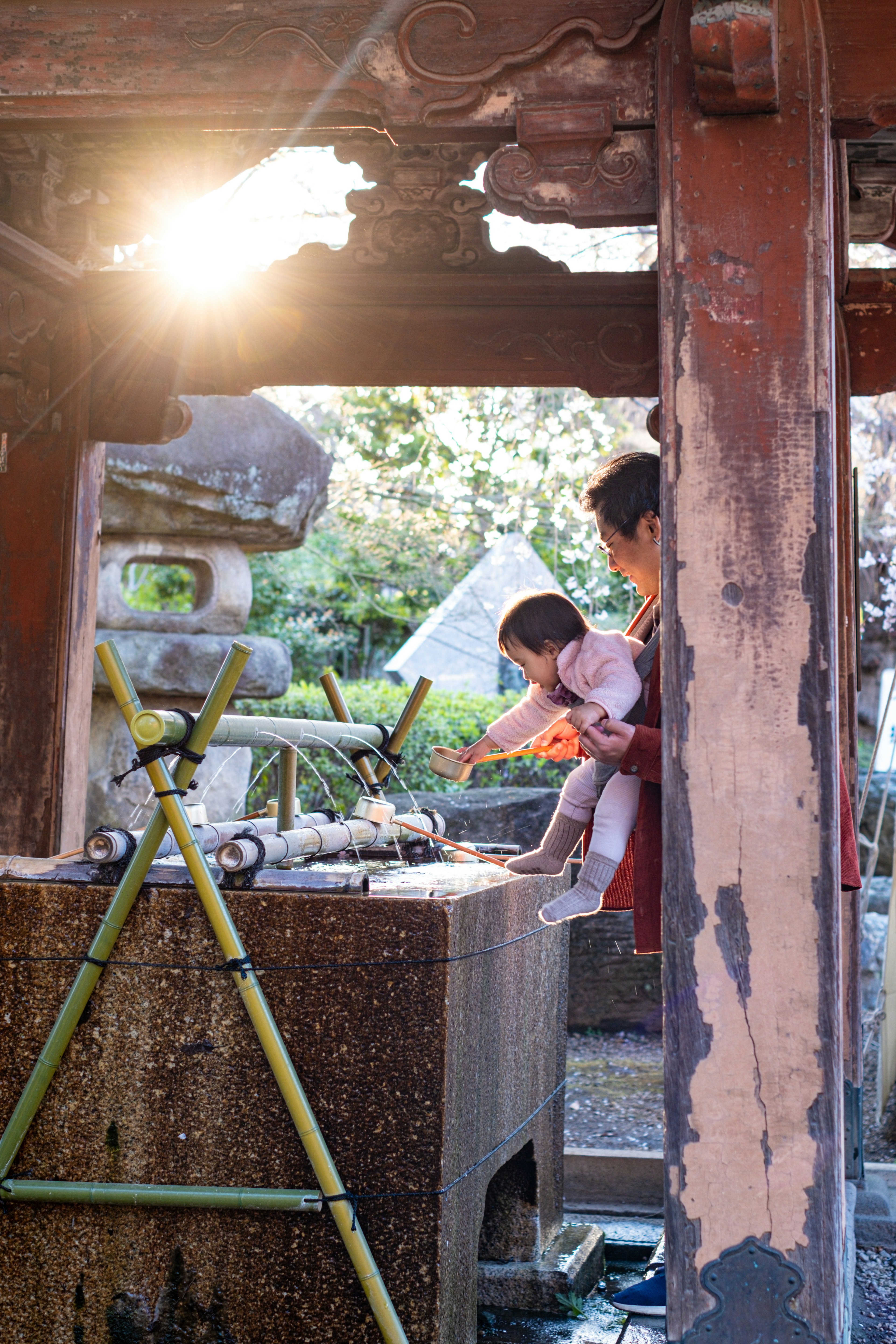 A child touching water at a purification fountain soft lighting with a stone lantern in the background