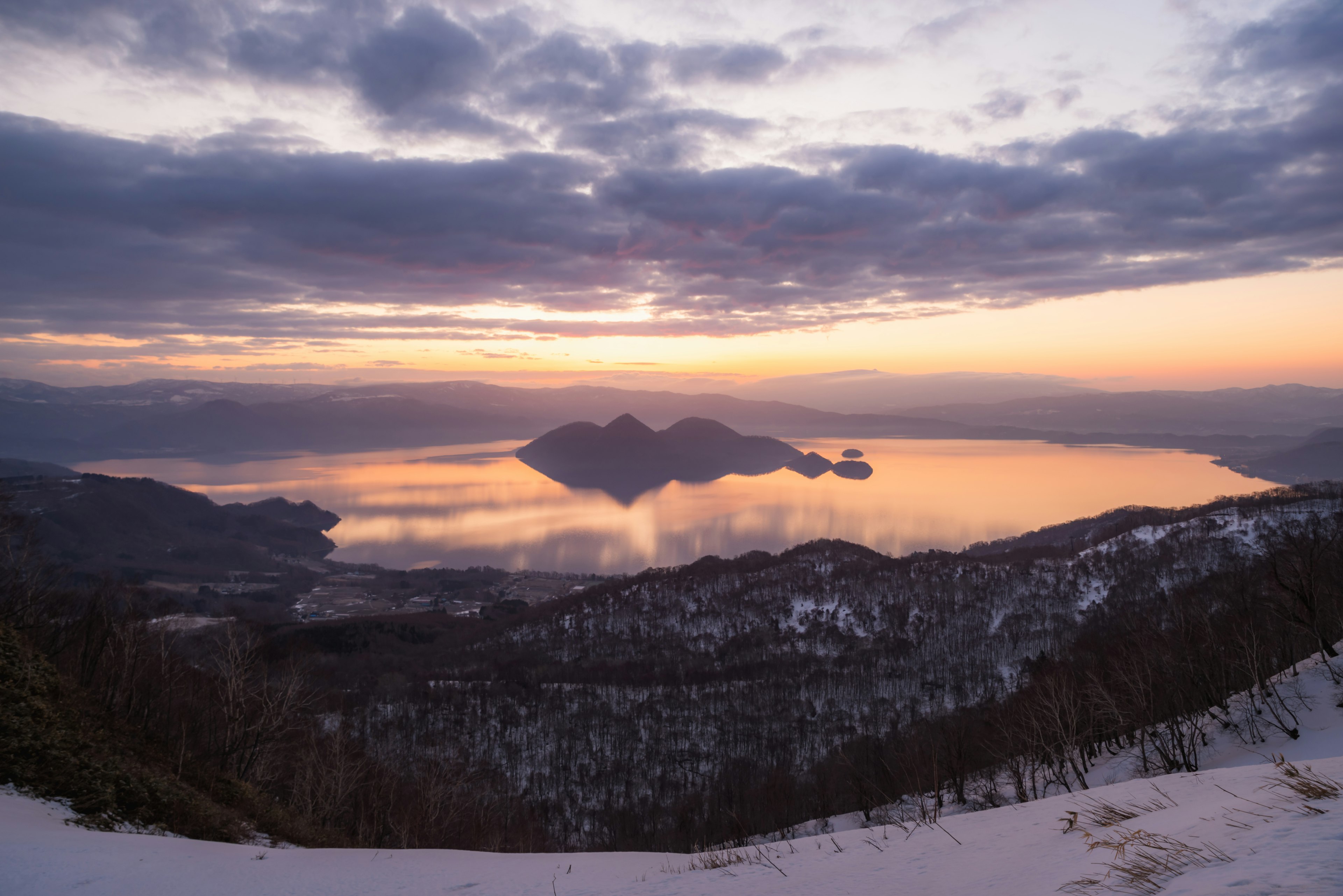 Vue du crépuscule sur un lac et des montagnes pentes enneigées et surface d'eau calme