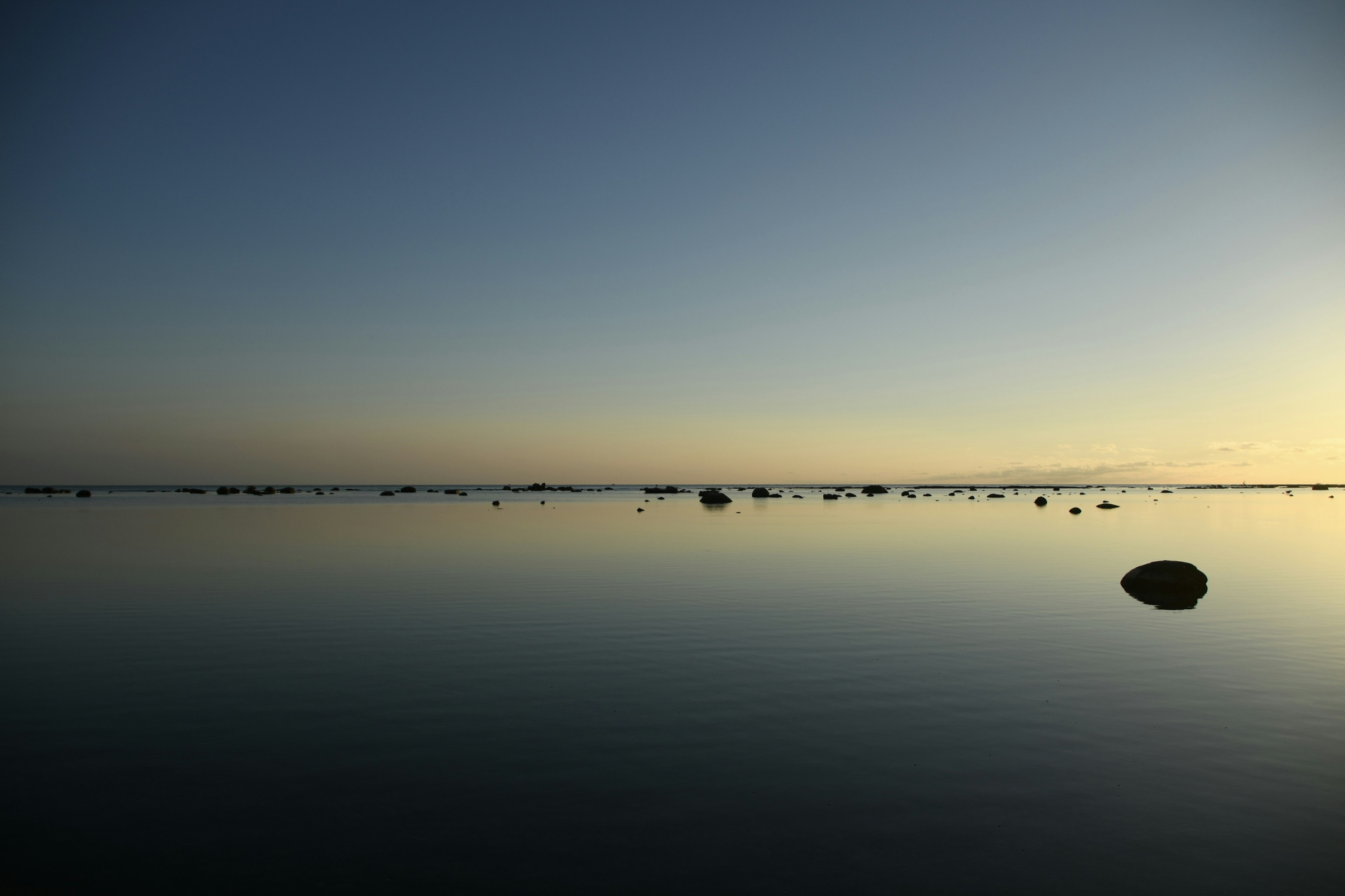 Superficie d'acqua calma con piccoli sassi al crepuscolo sul mare