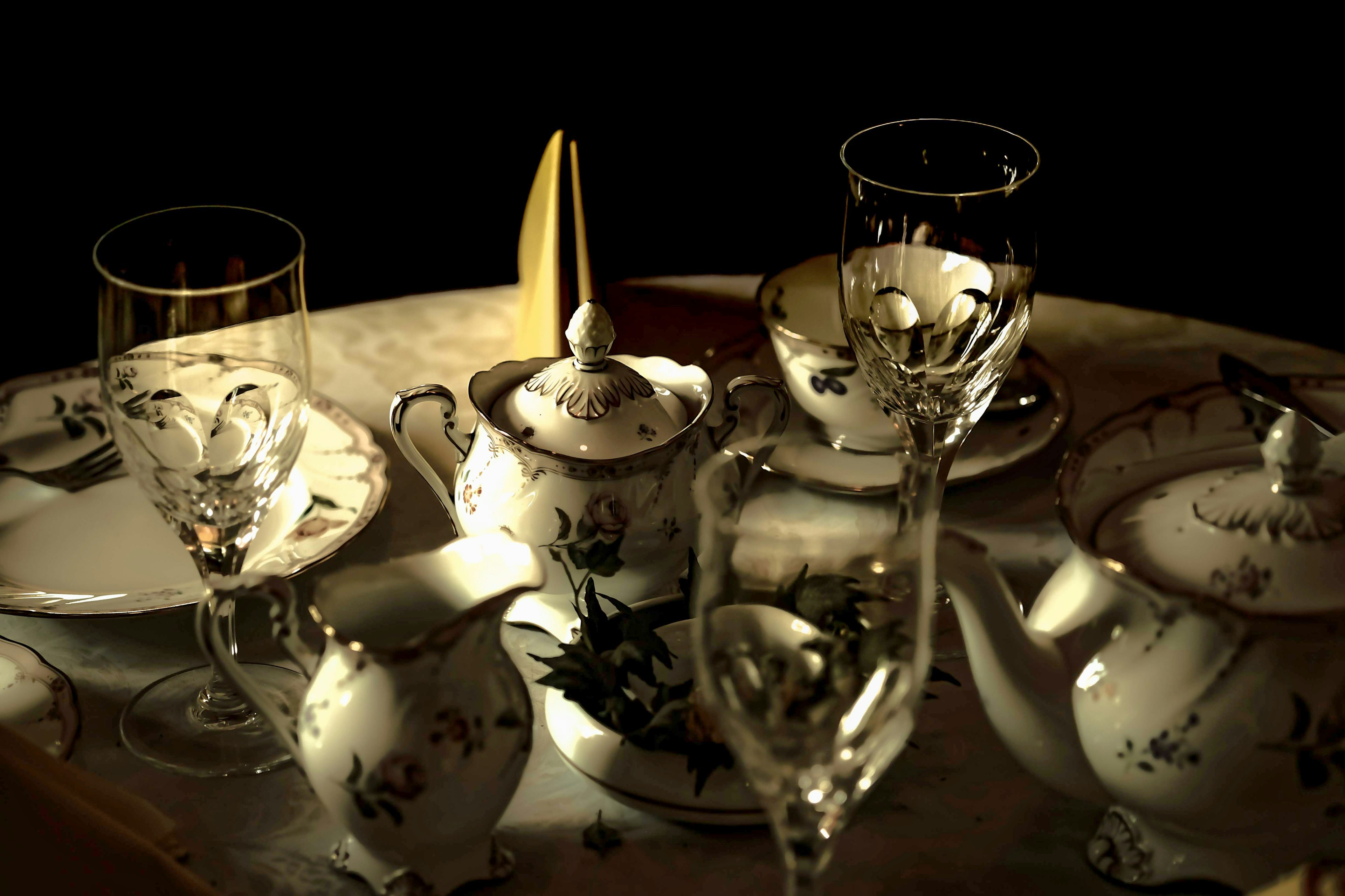 A scene of a white porcelain tea set and crystal glasses on a table