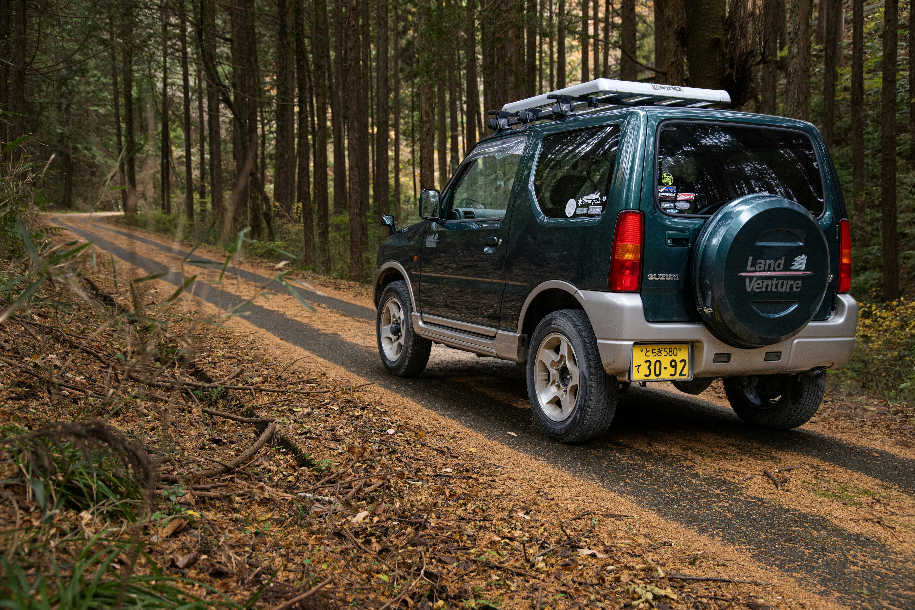 A green SUV driving on a dirt path through the forest