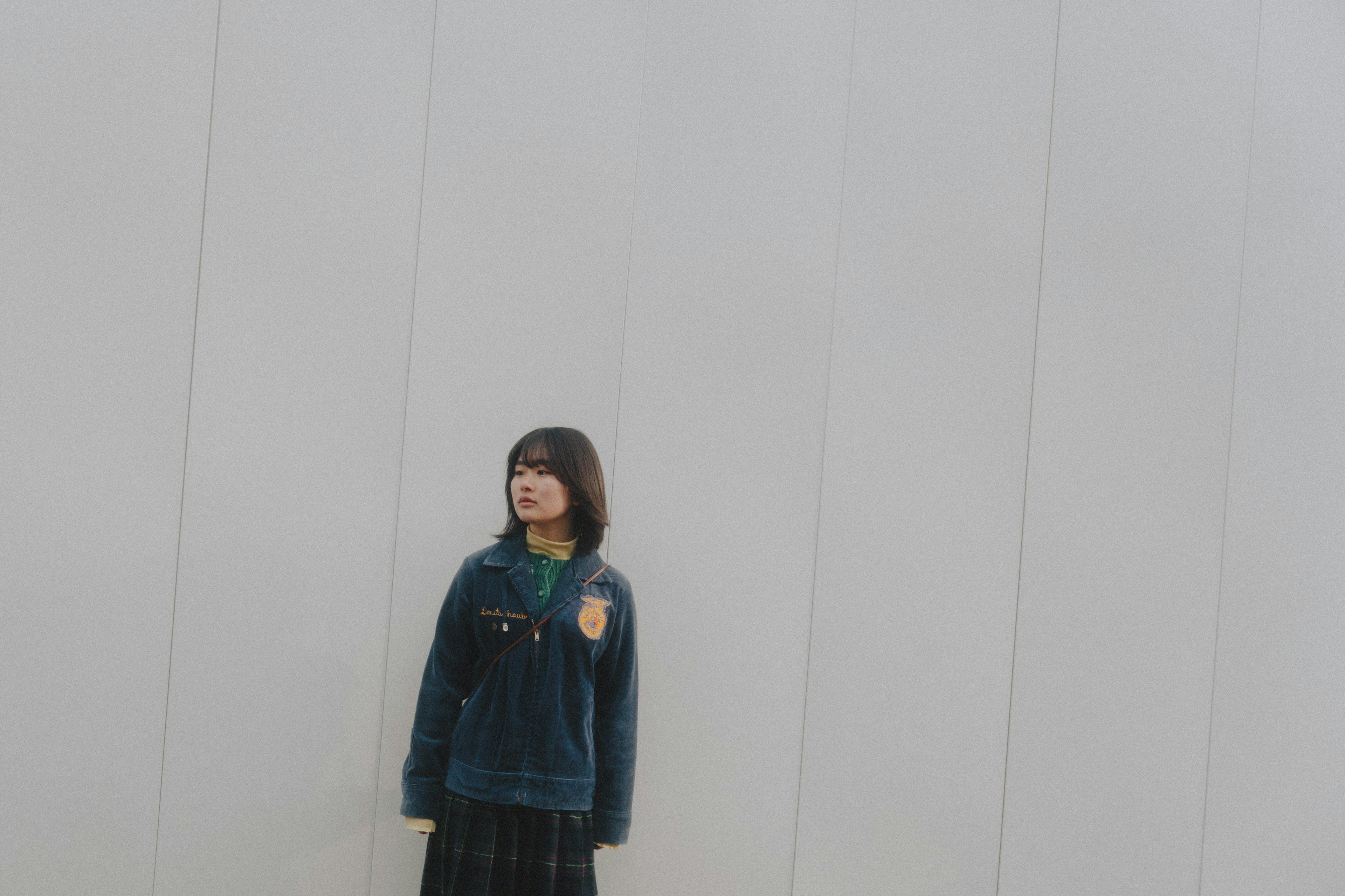 Young woman standing in front of a white wall wearing a blue jacket and a black skirt