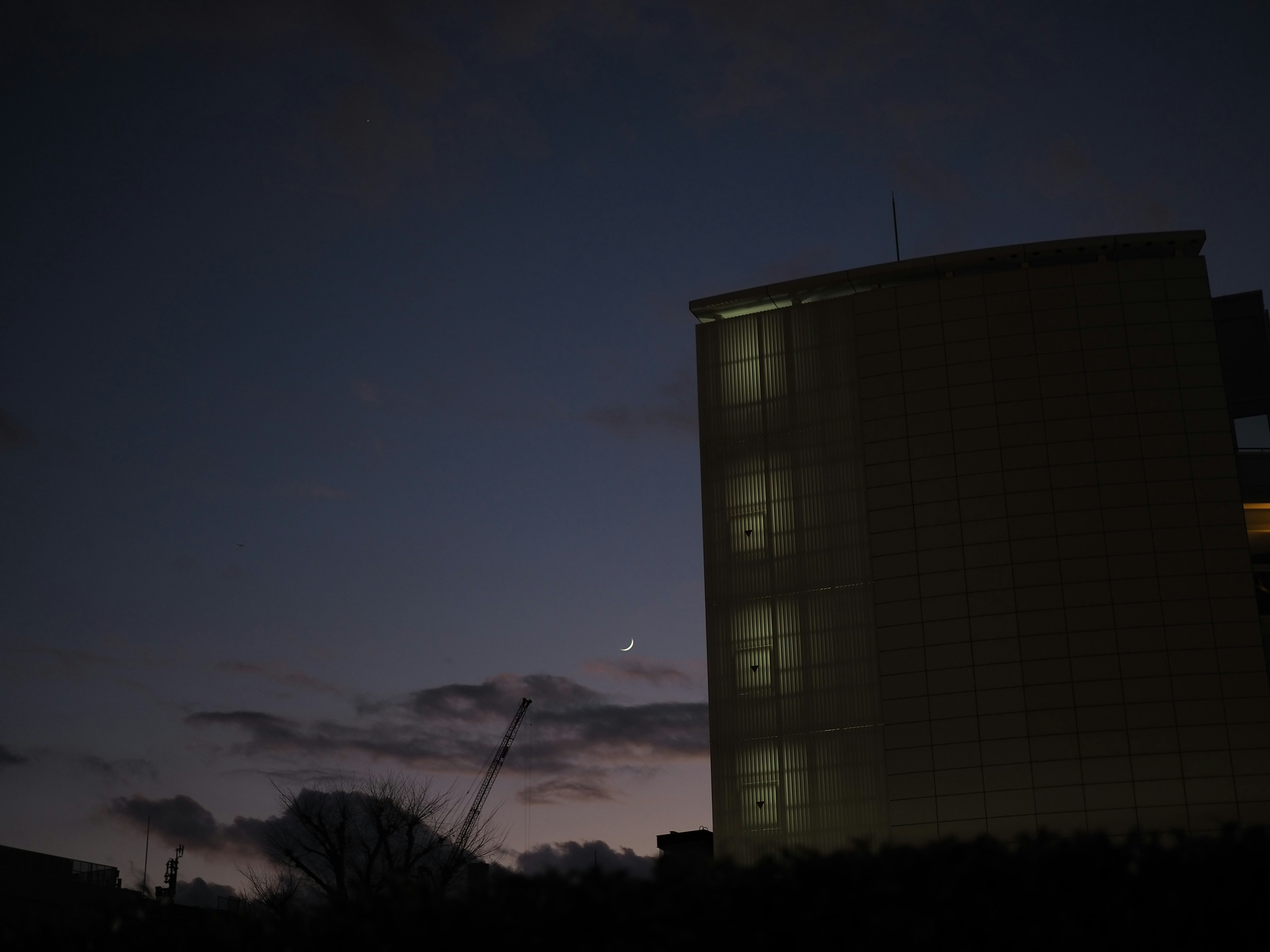 夜空に浮かぶ月と薄明かりの建物が見える