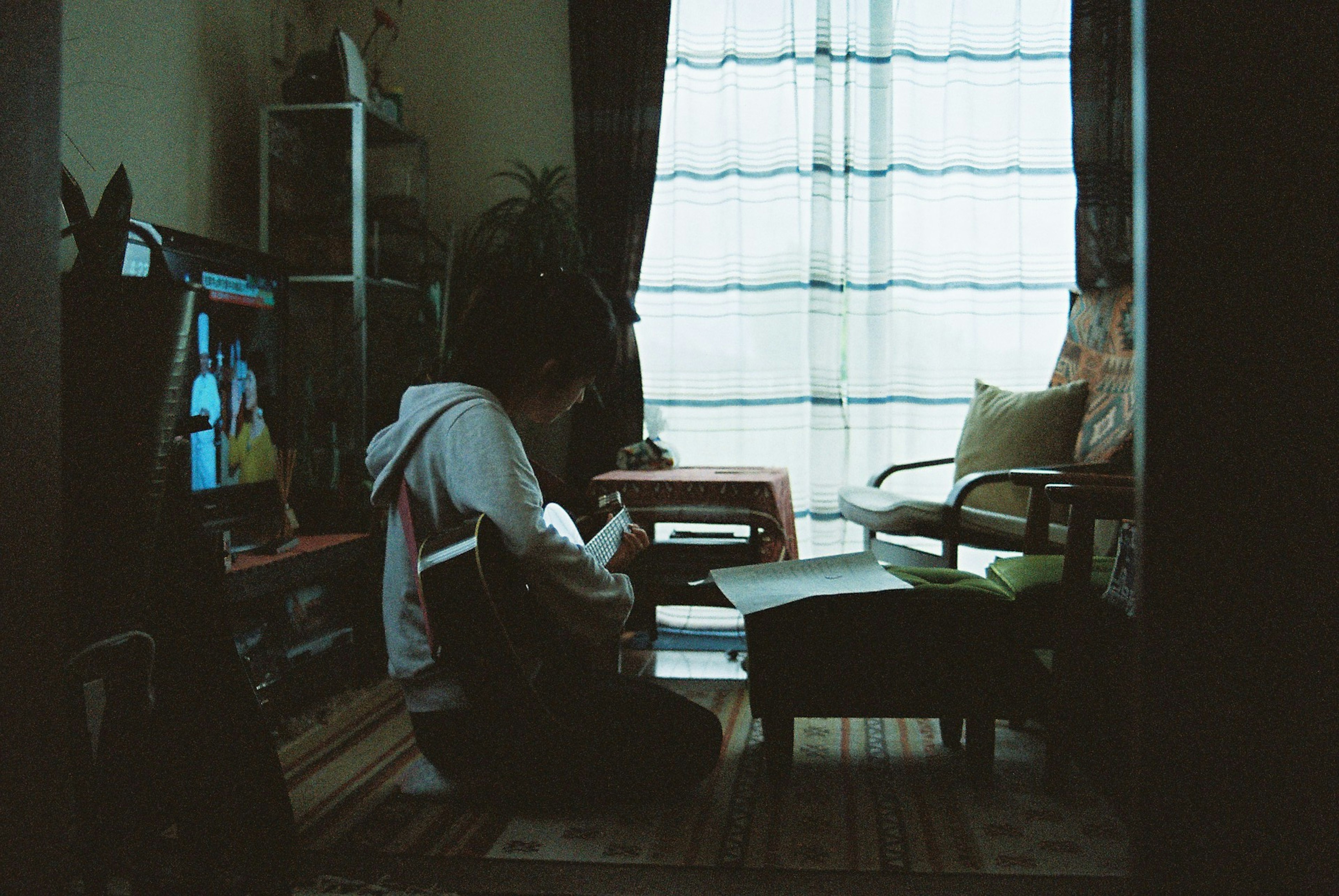 Person sitting on the floor playing guitar near a window with natural light