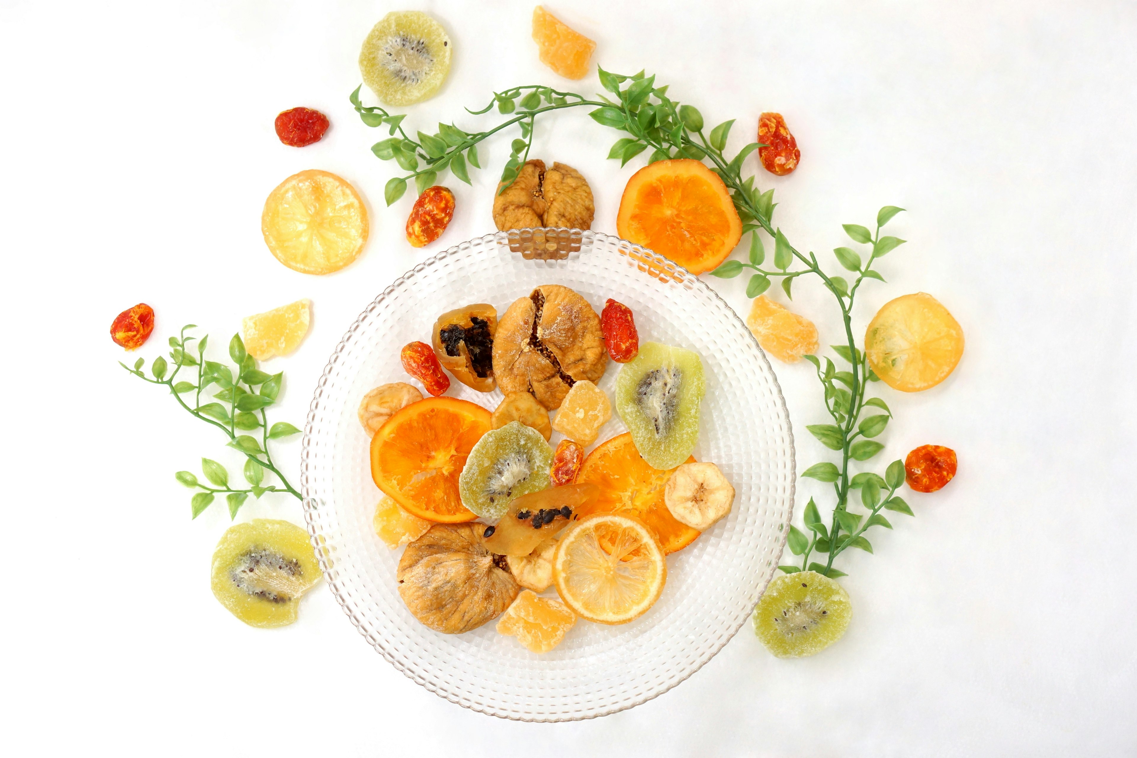 A beautifully arranged plate of colorful dried fruits surrounded by green leaves