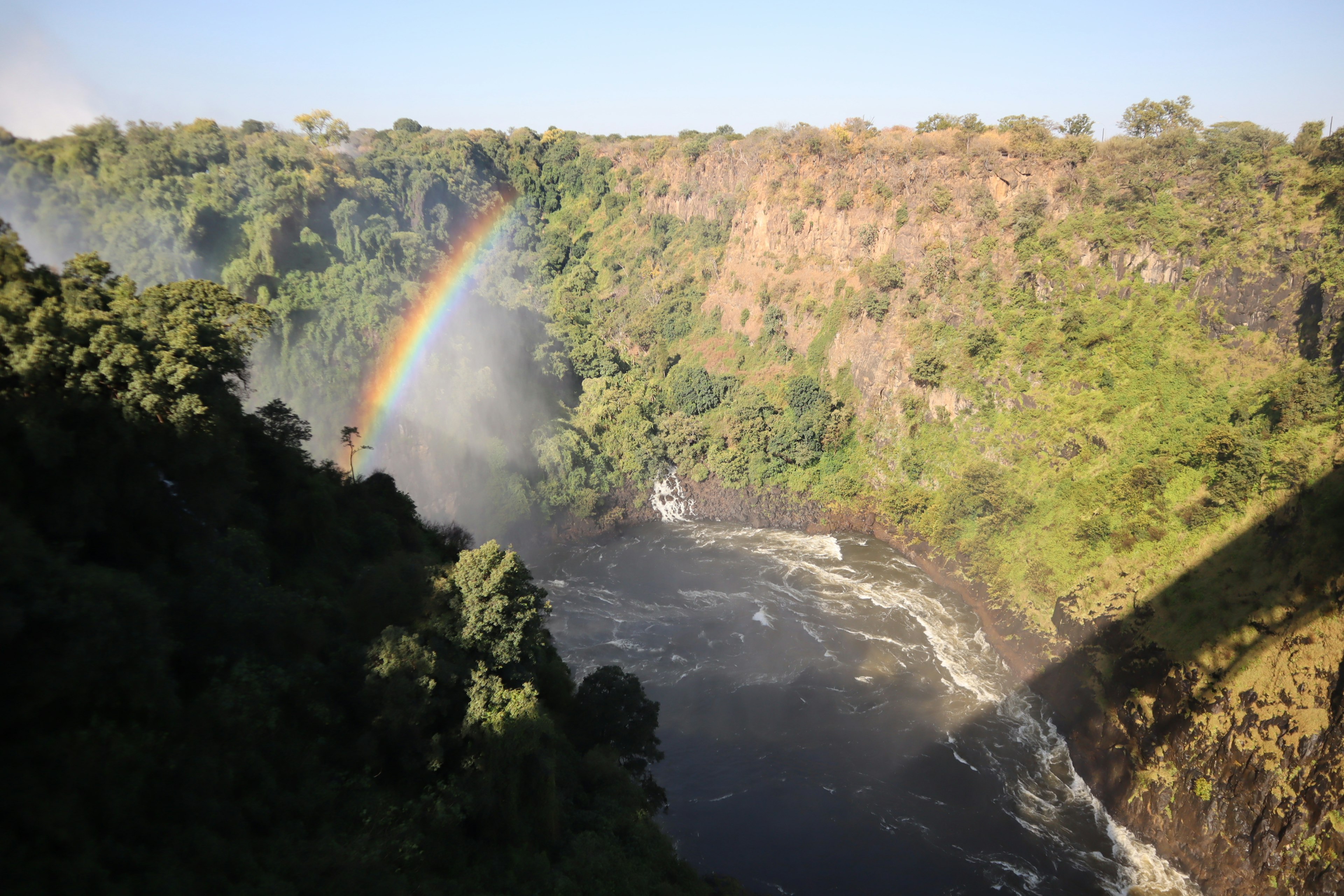 Scenic view of a waterfall and rainbow over a lush green canyon