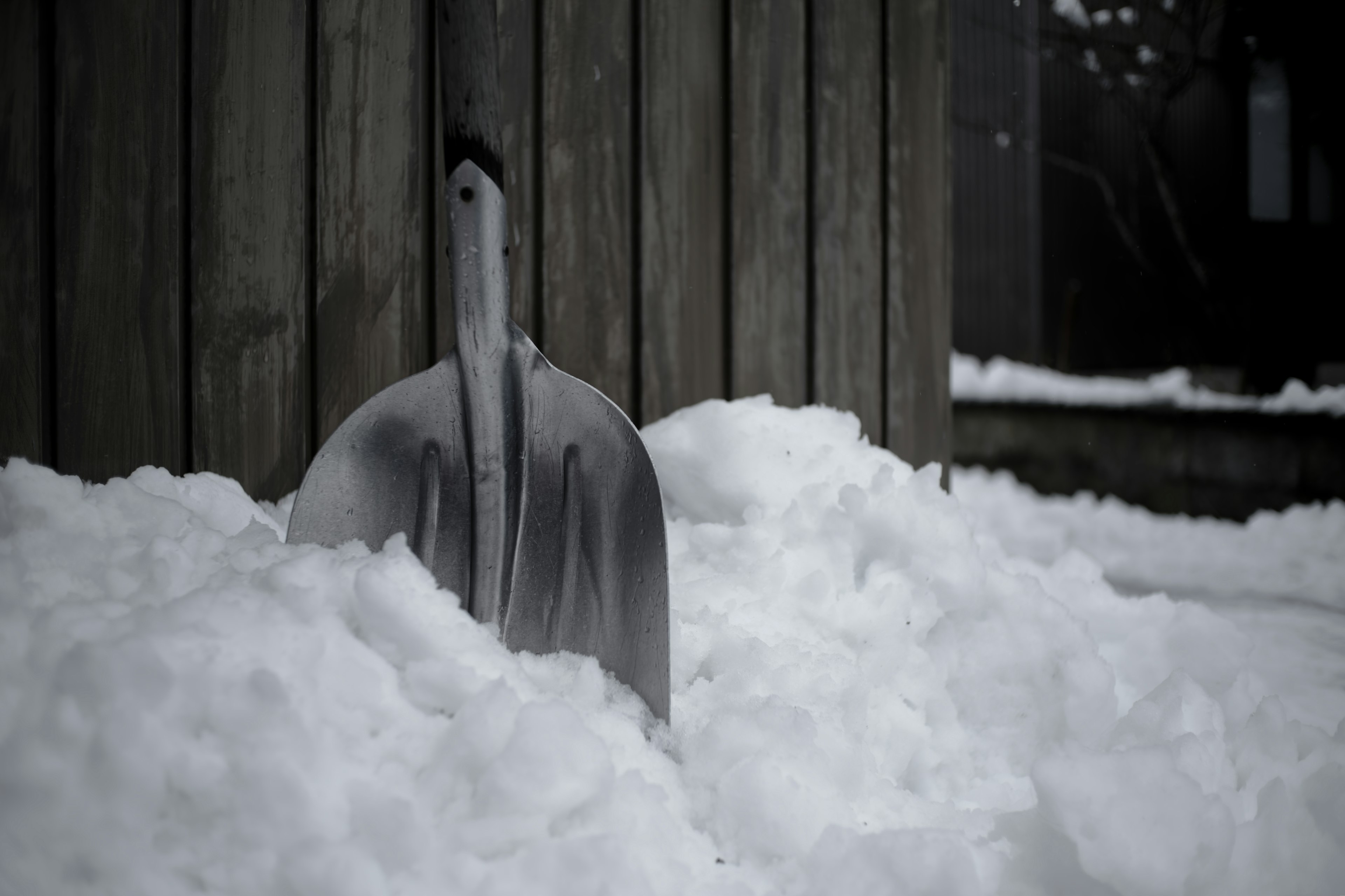 Shovel buried in snow next to wooden wall