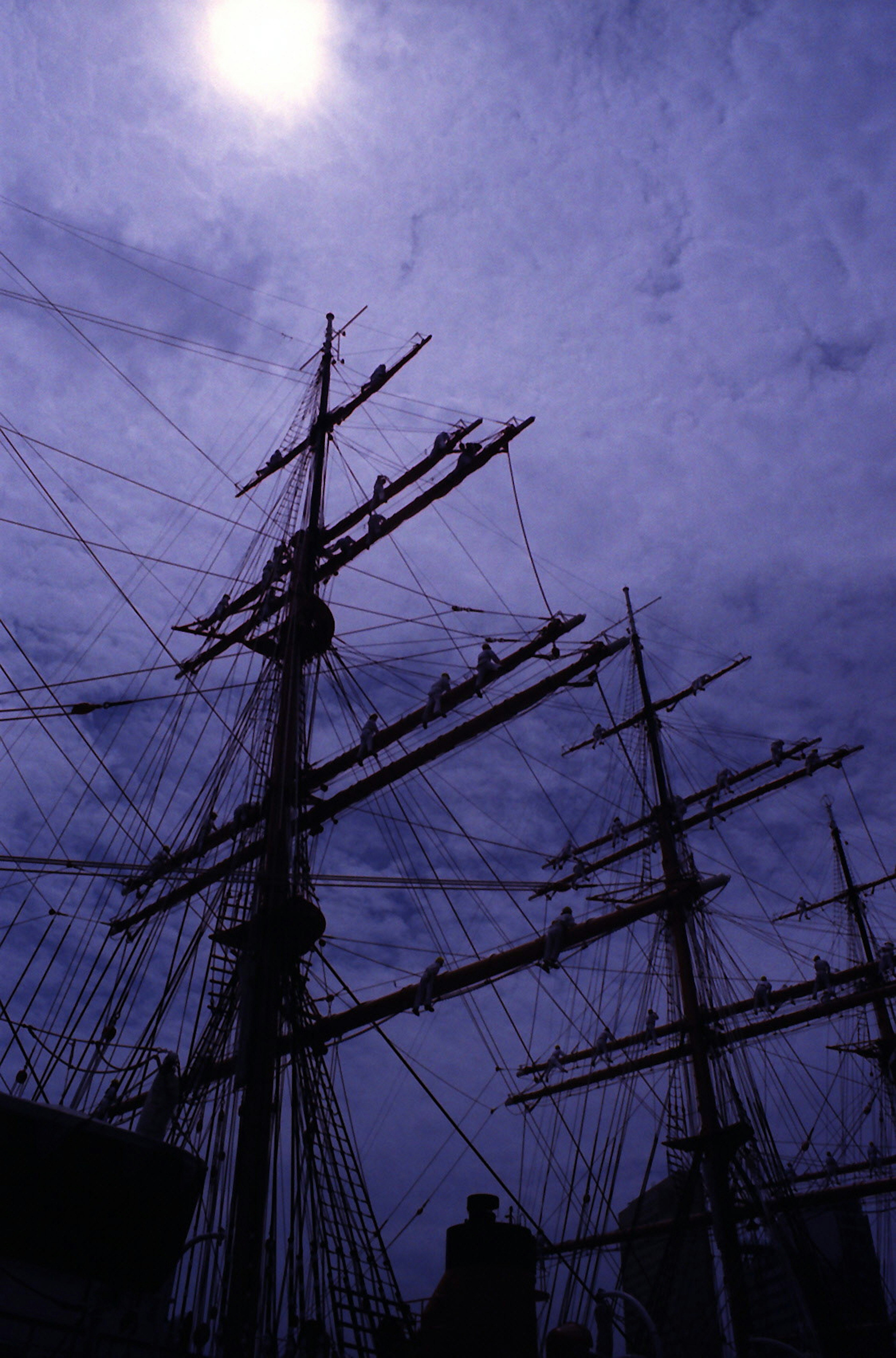 Mast di nave in silhouette contro un cielo scuro con un sole luminoso