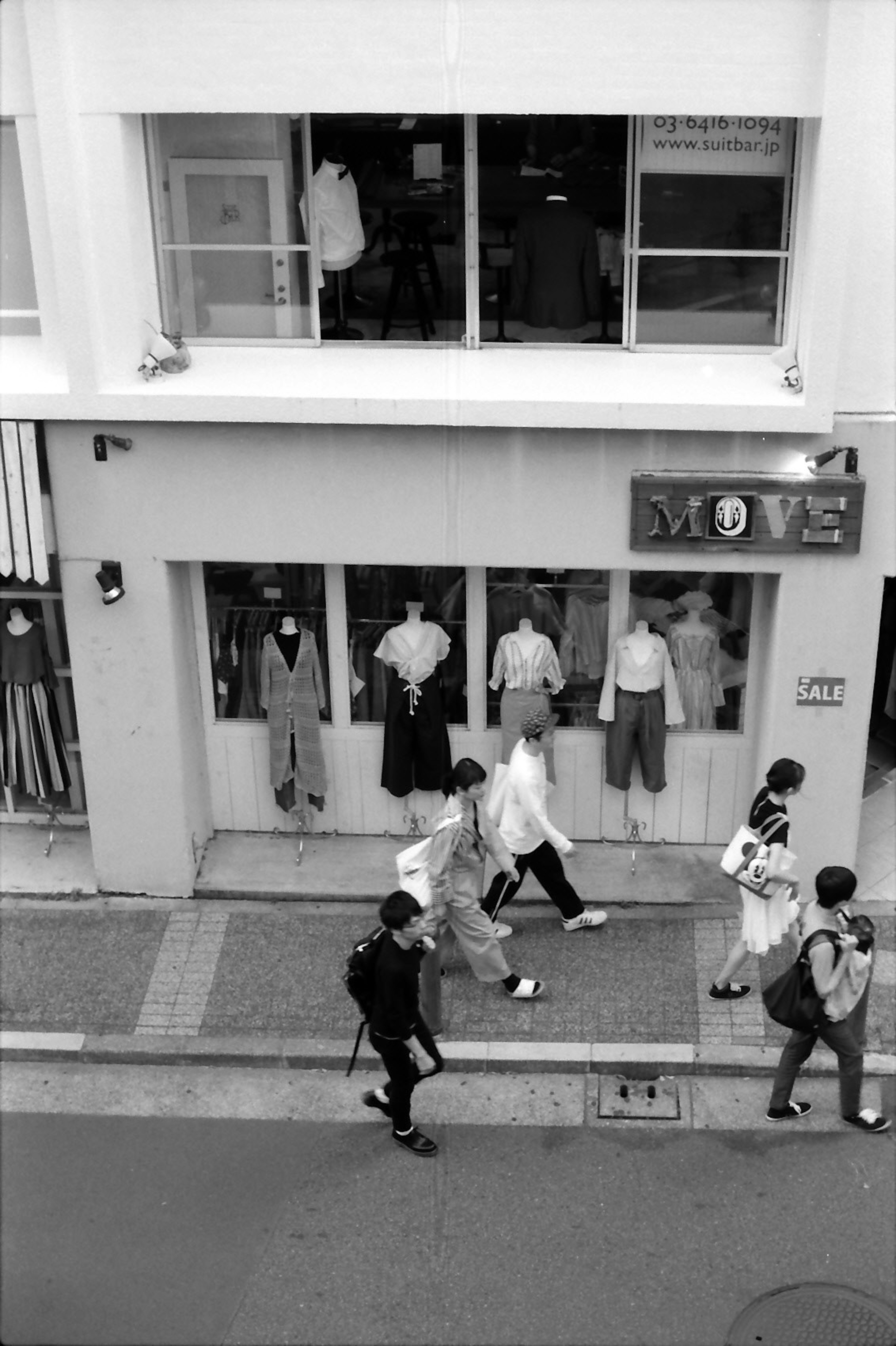 Escena de calle en blanco y negro con peatones y ropa exhibida en las ventanas