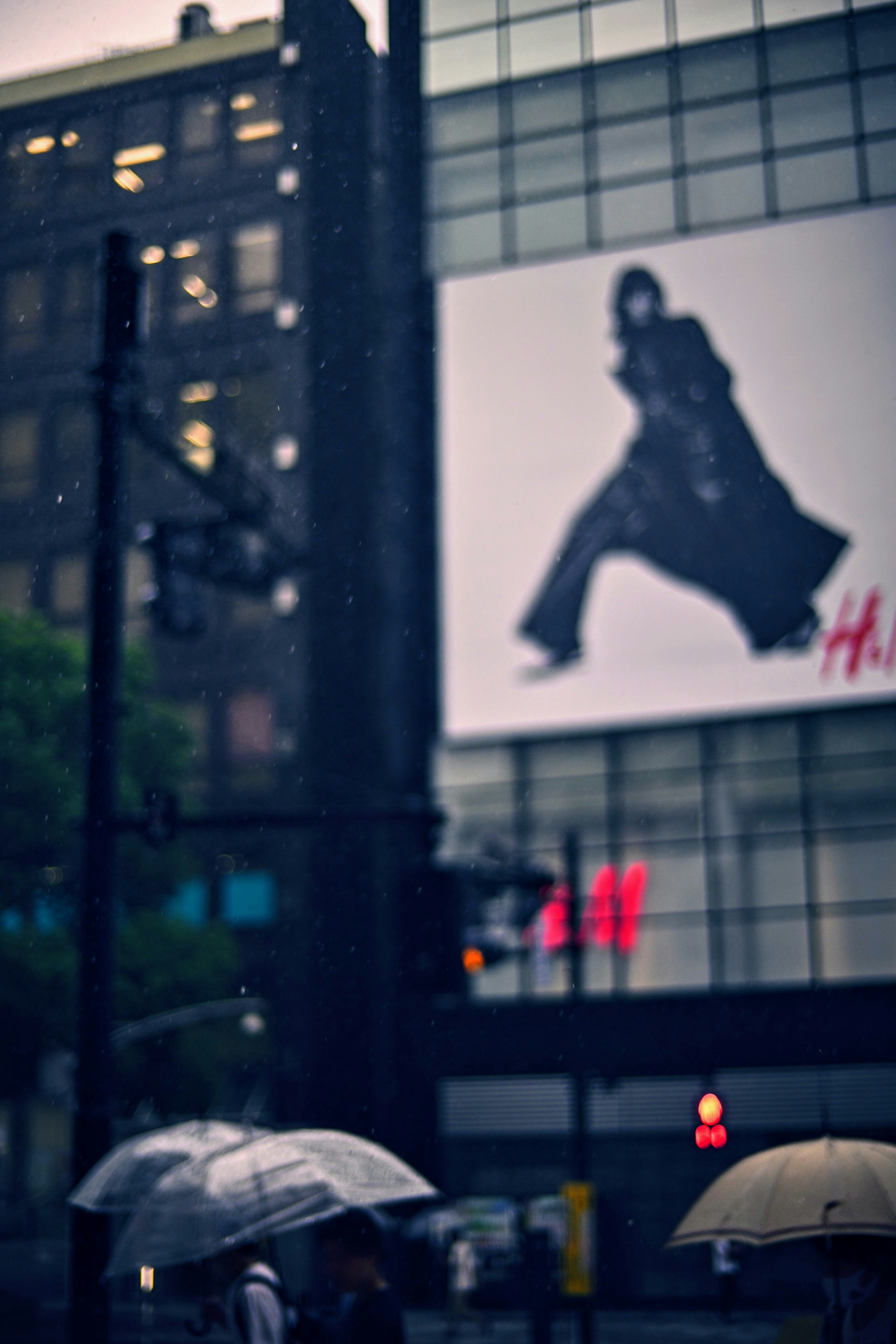 Escena urbana con personas sosteniendo paraguas y un anuncio de H&M bajo la lluvia