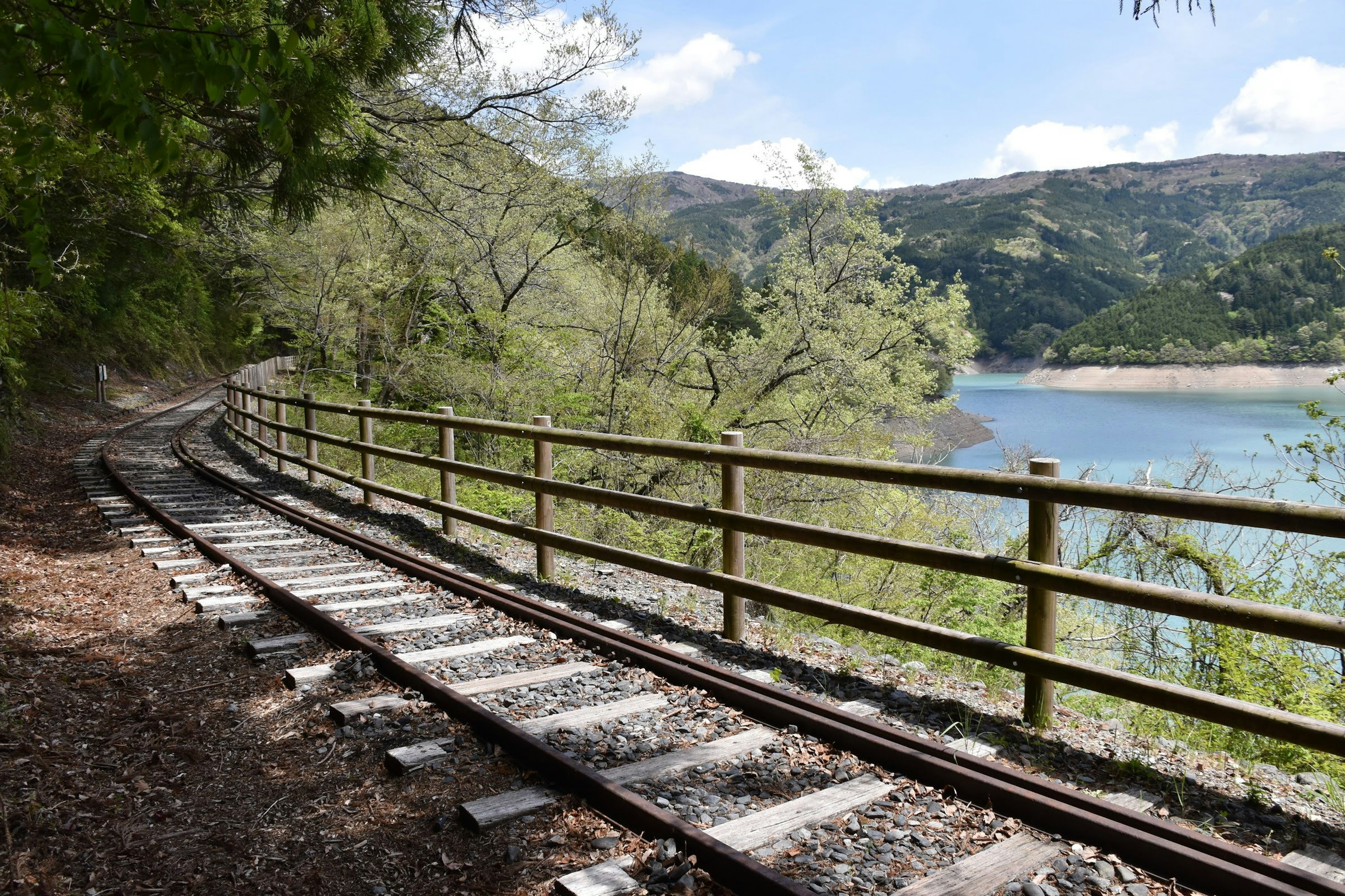 Curved railway tracks near a lake with a wooden fence