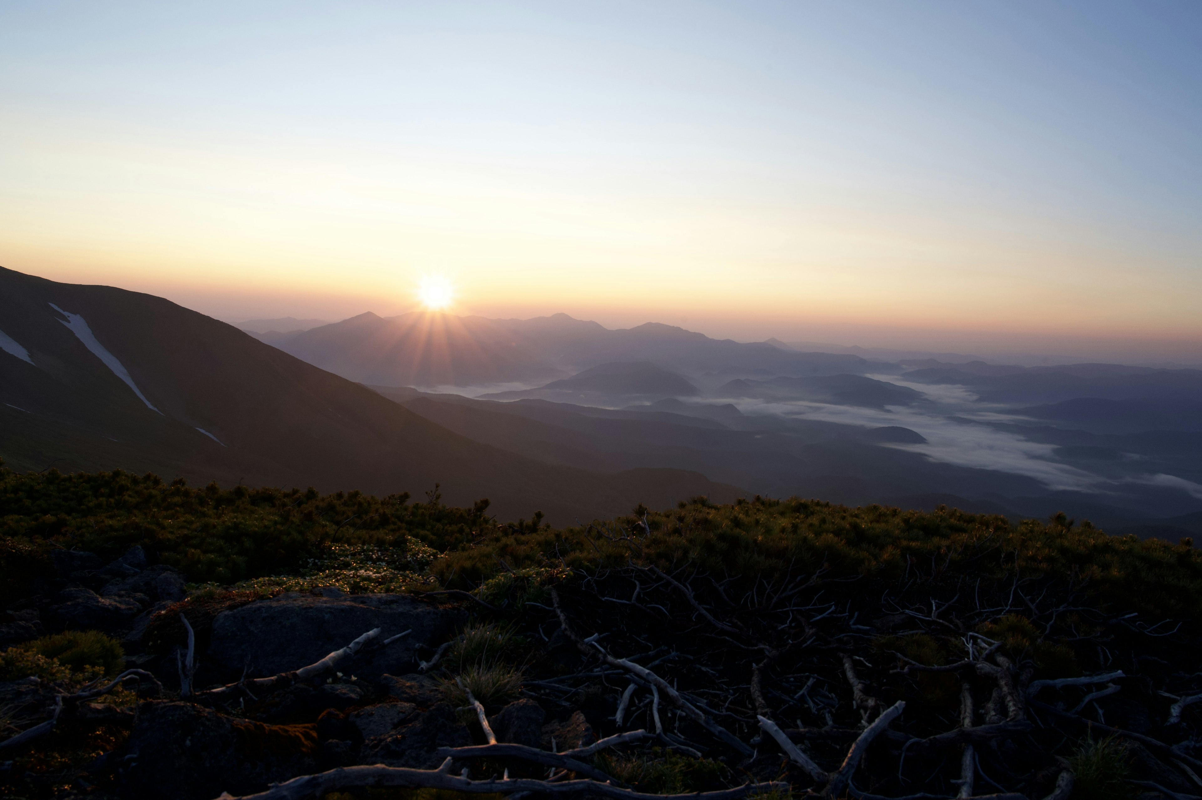 Pemandangan matahari terbit dari puncak gunung dengan lembah berkabut dan pegunungan jauh