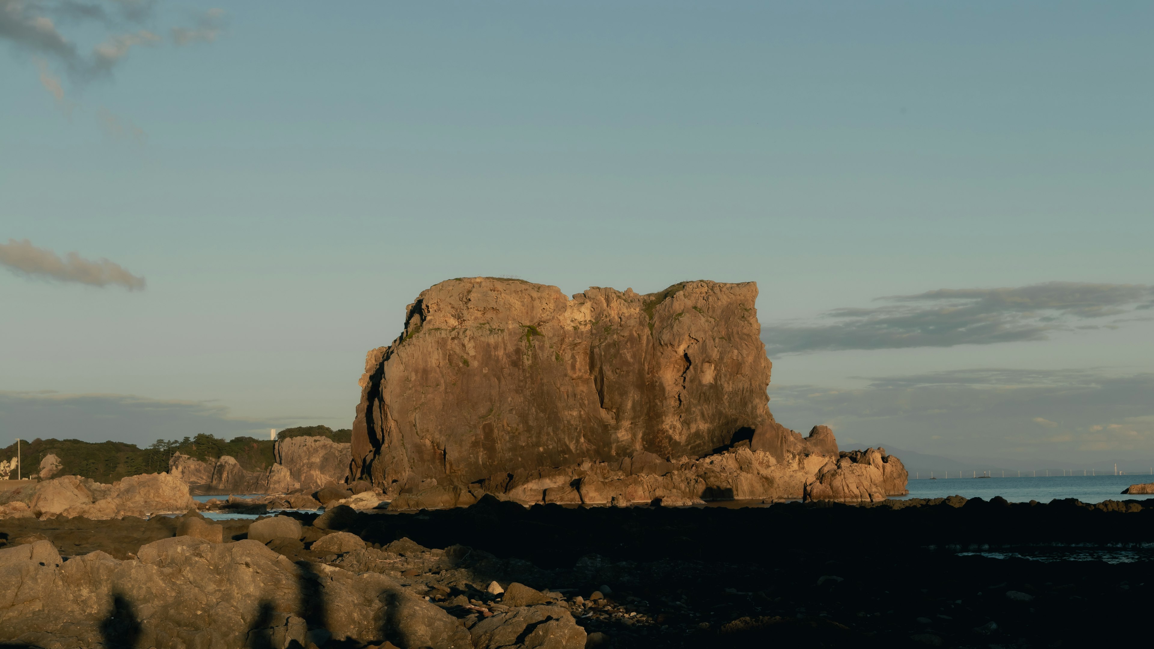 A large rock formation rising from the coast with a clear blue sky