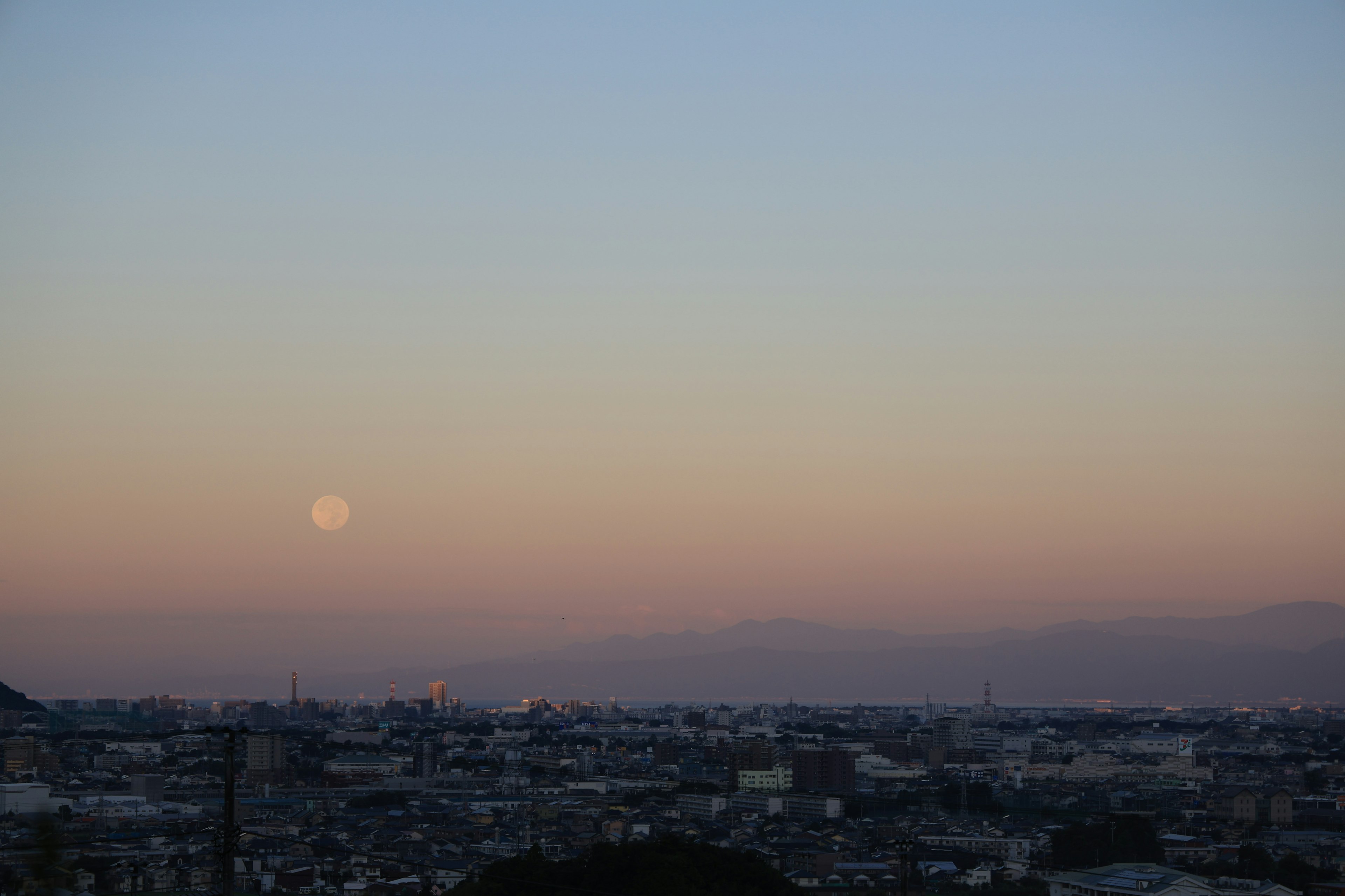 Horizonte urbano al atardecer con luna visible y suaves colores pastel