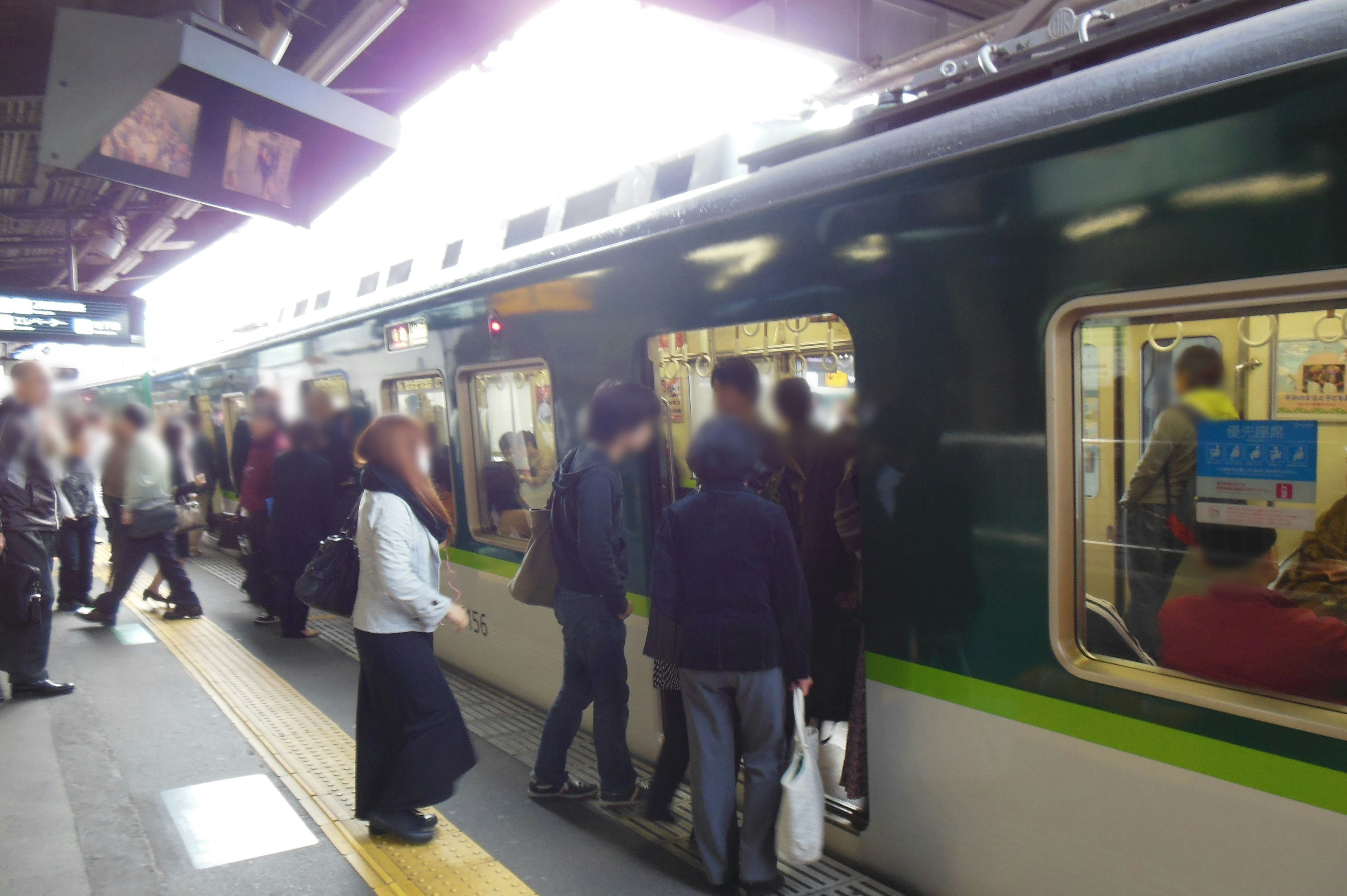 混雑した駅で電車に乗り込む人々と緑色の電車