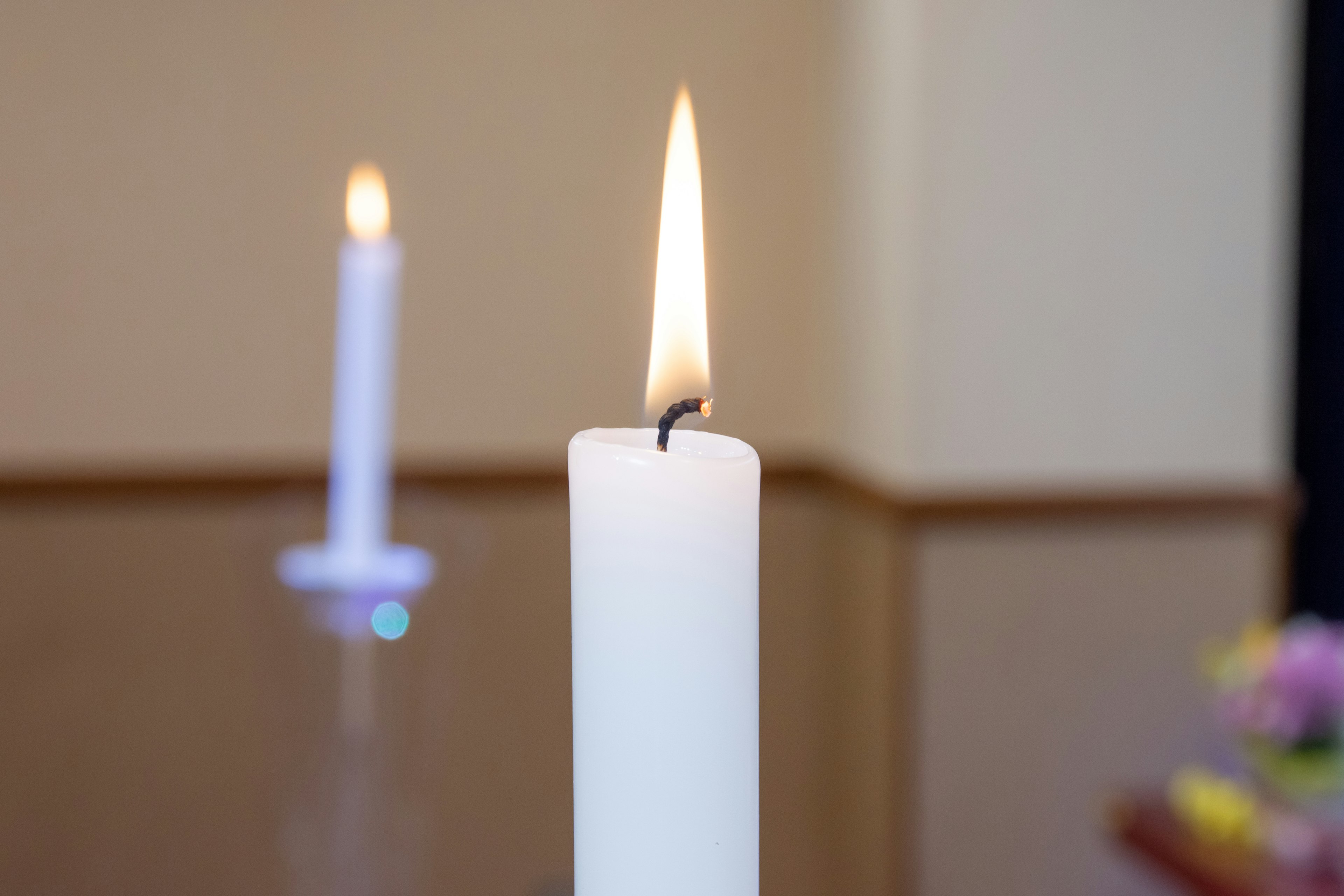 A white candle burning with a blurred candle in the background