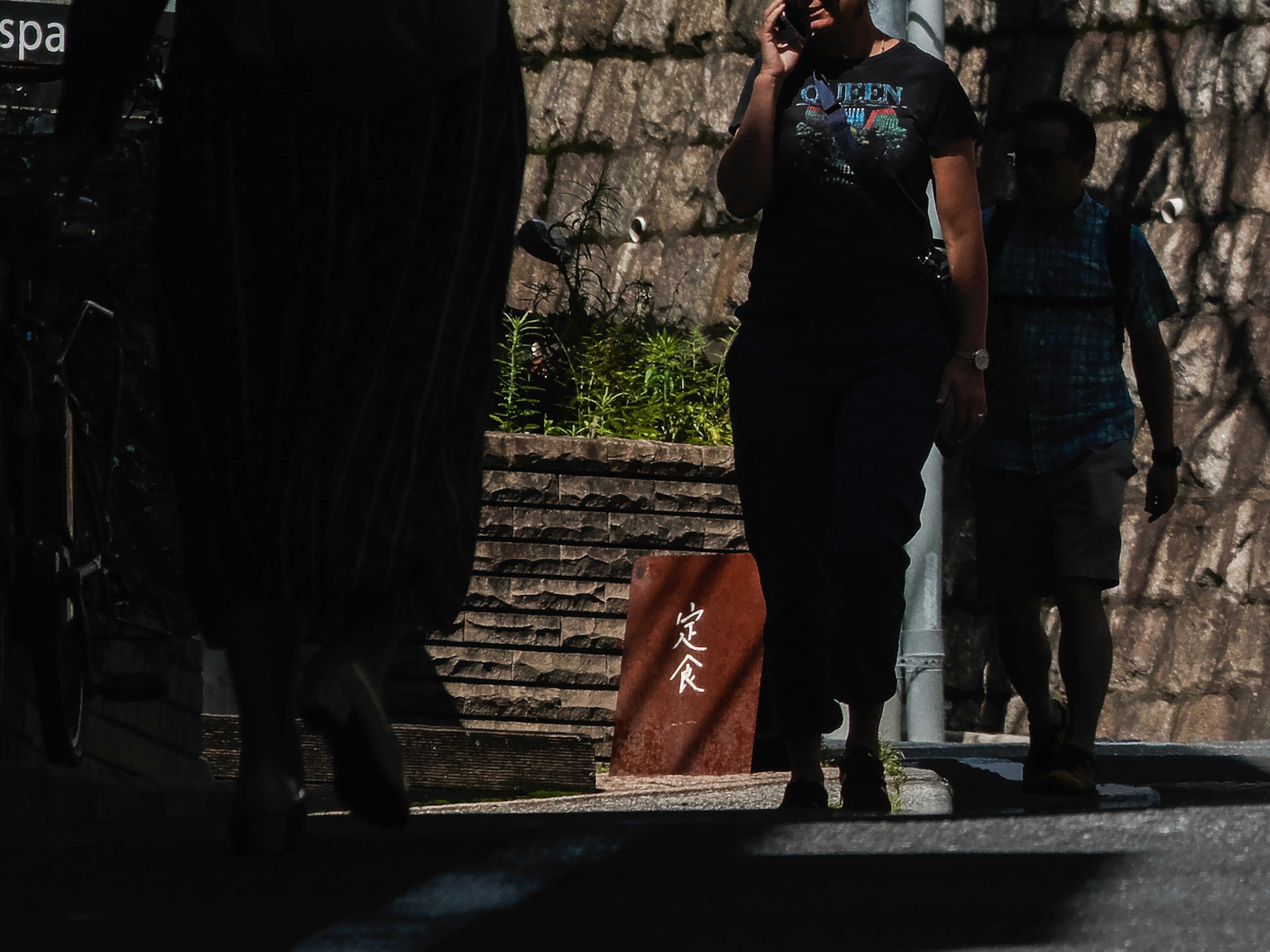 Personas caminando a la sombra con un muro de piedra de fondo