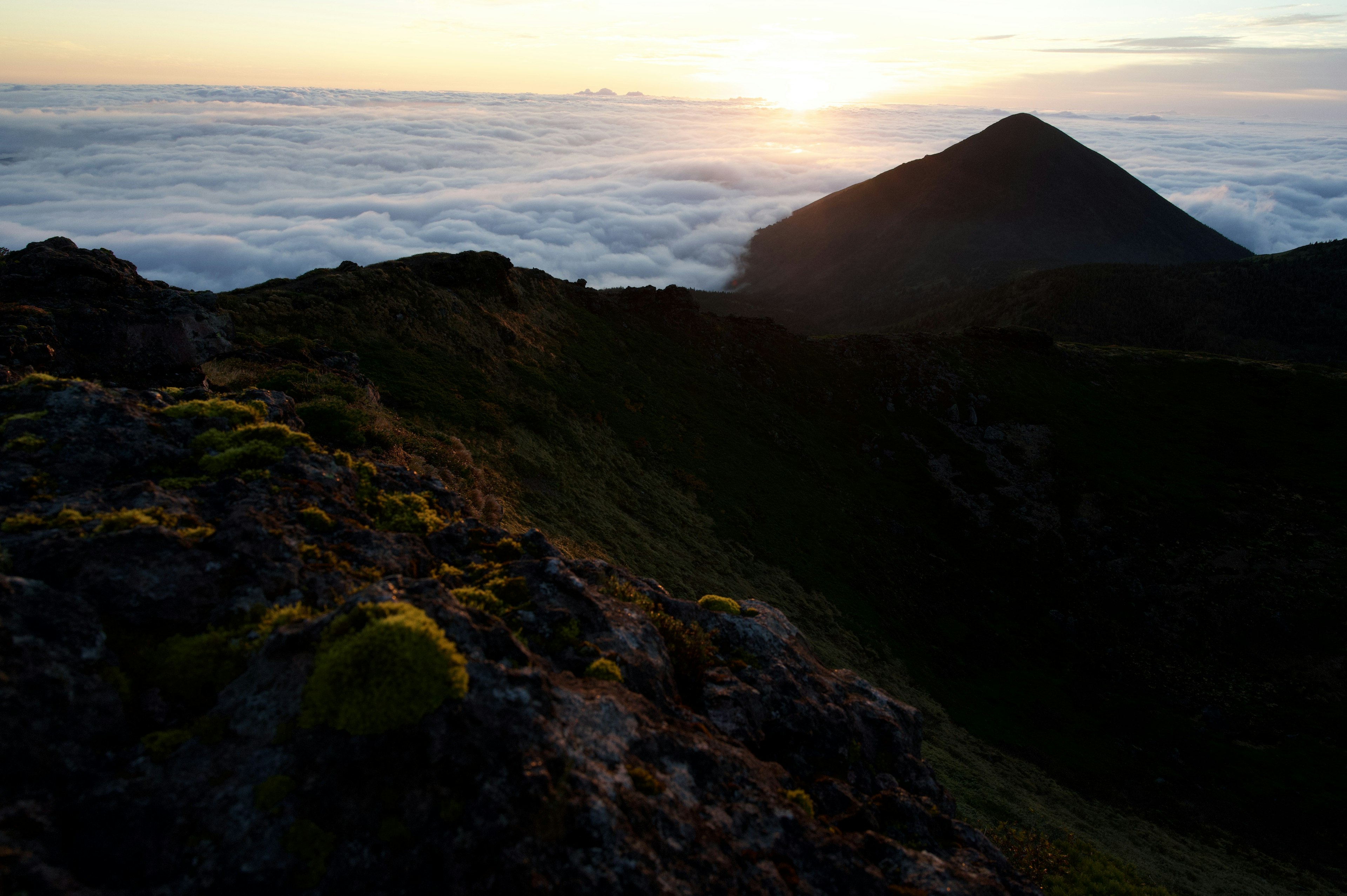 夕日が雲海の上に沈む風景で緑の苔が岩に生えた山の斜面