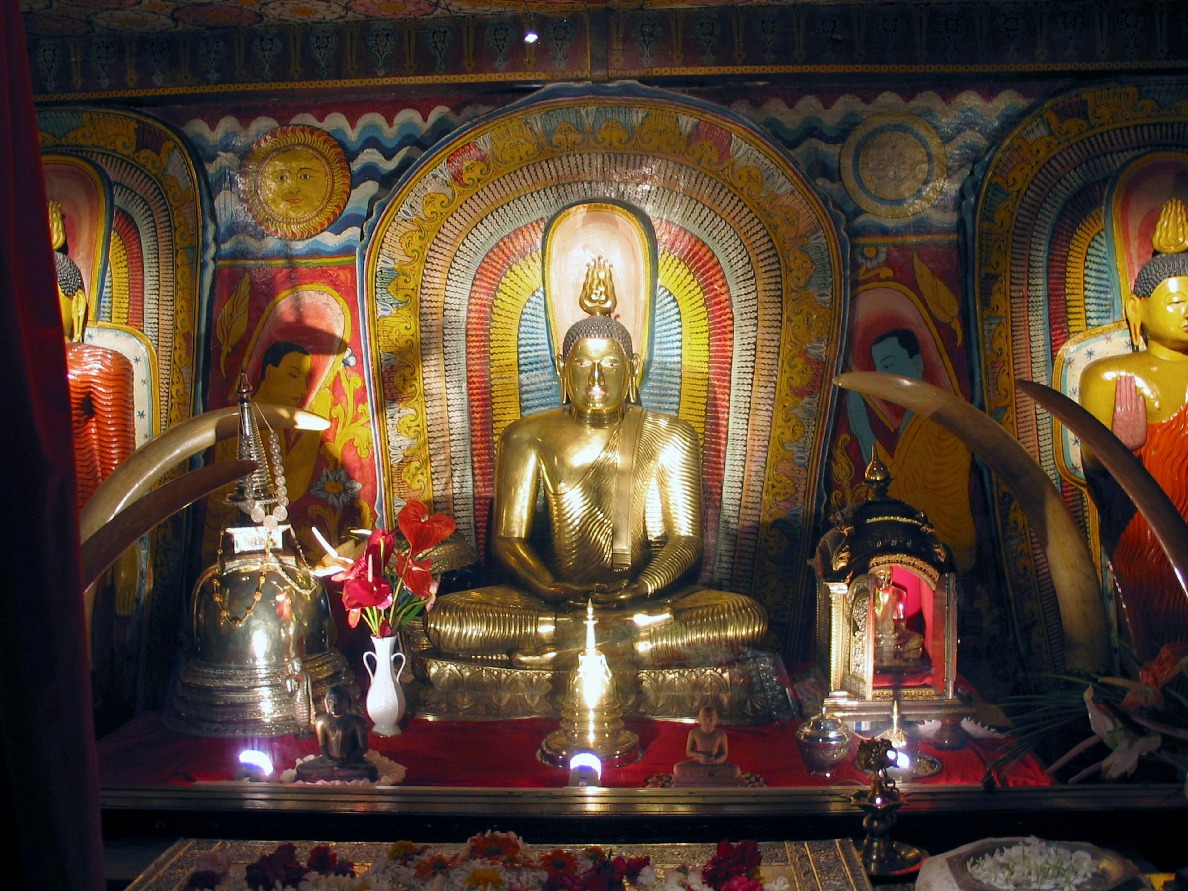 Goldene Buddha-Statue in der Mitte mit bunten Wandmalereien im Hintergrund