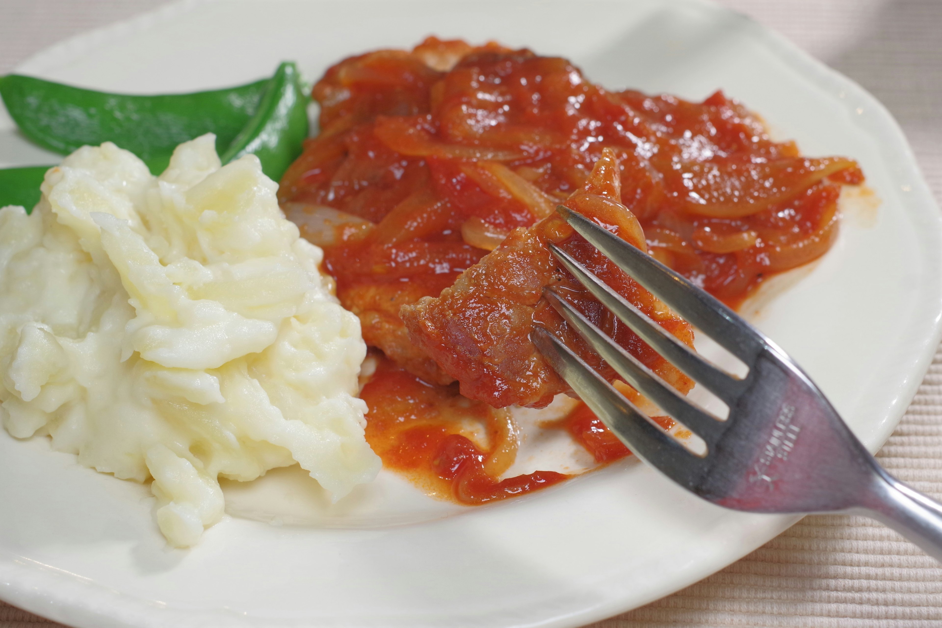 Plate with tomato sauce meat dish mashed potatoes and snap peas