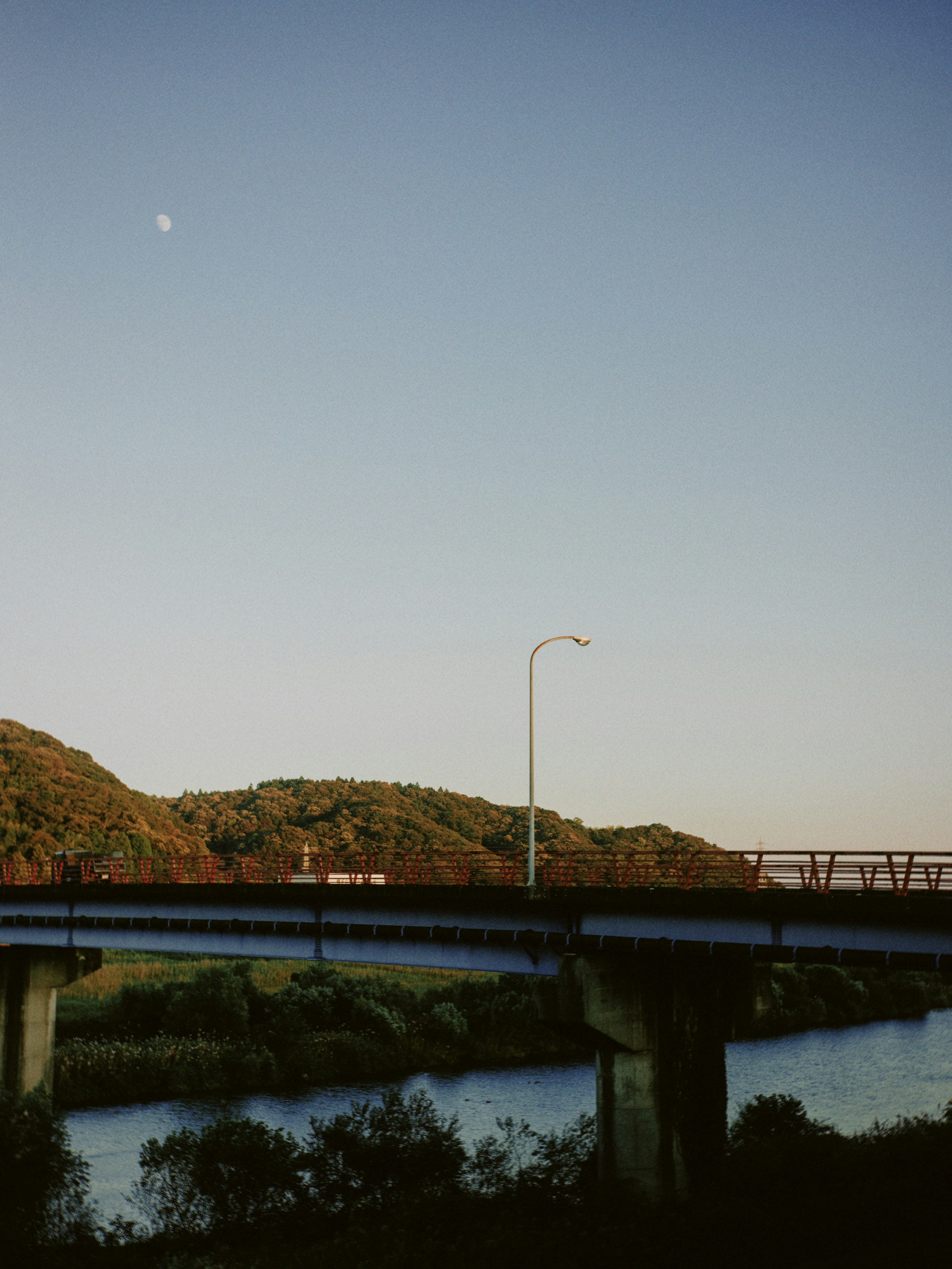 Puente sobre un río con una luna visible en el cielo