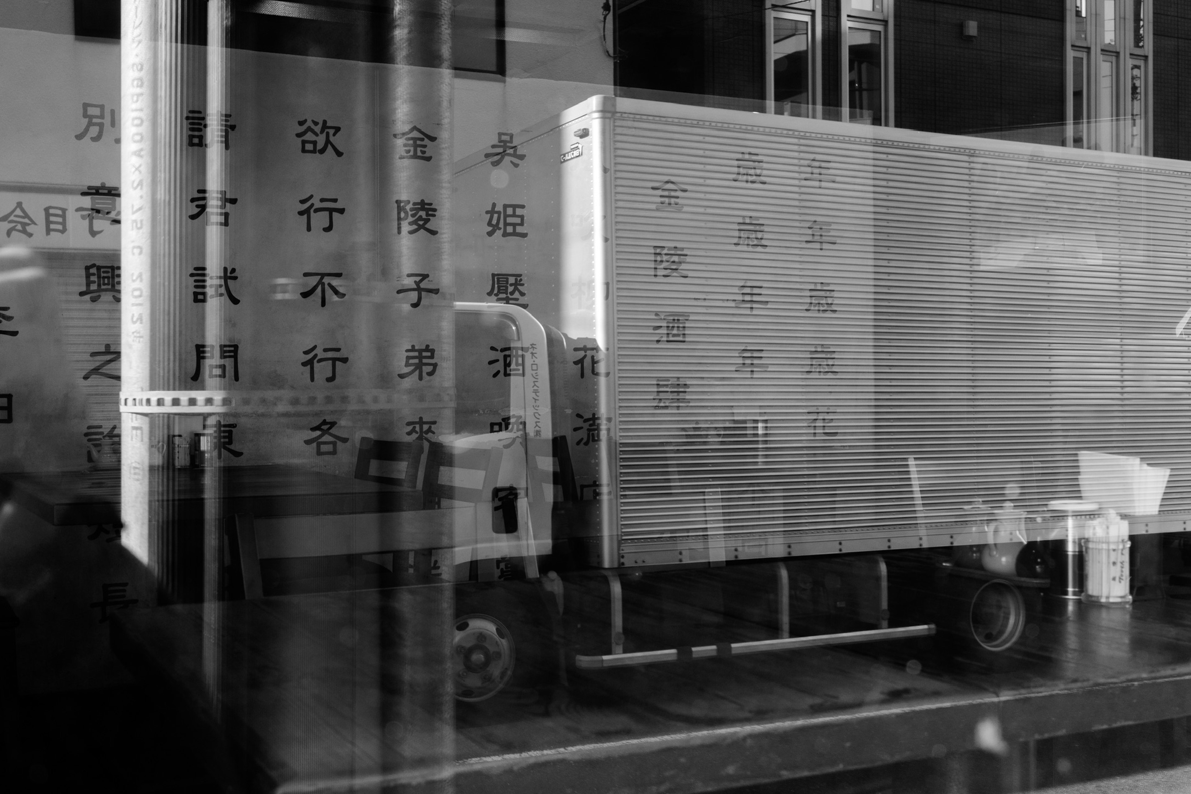 A black and white image of a truck reflected in a building window