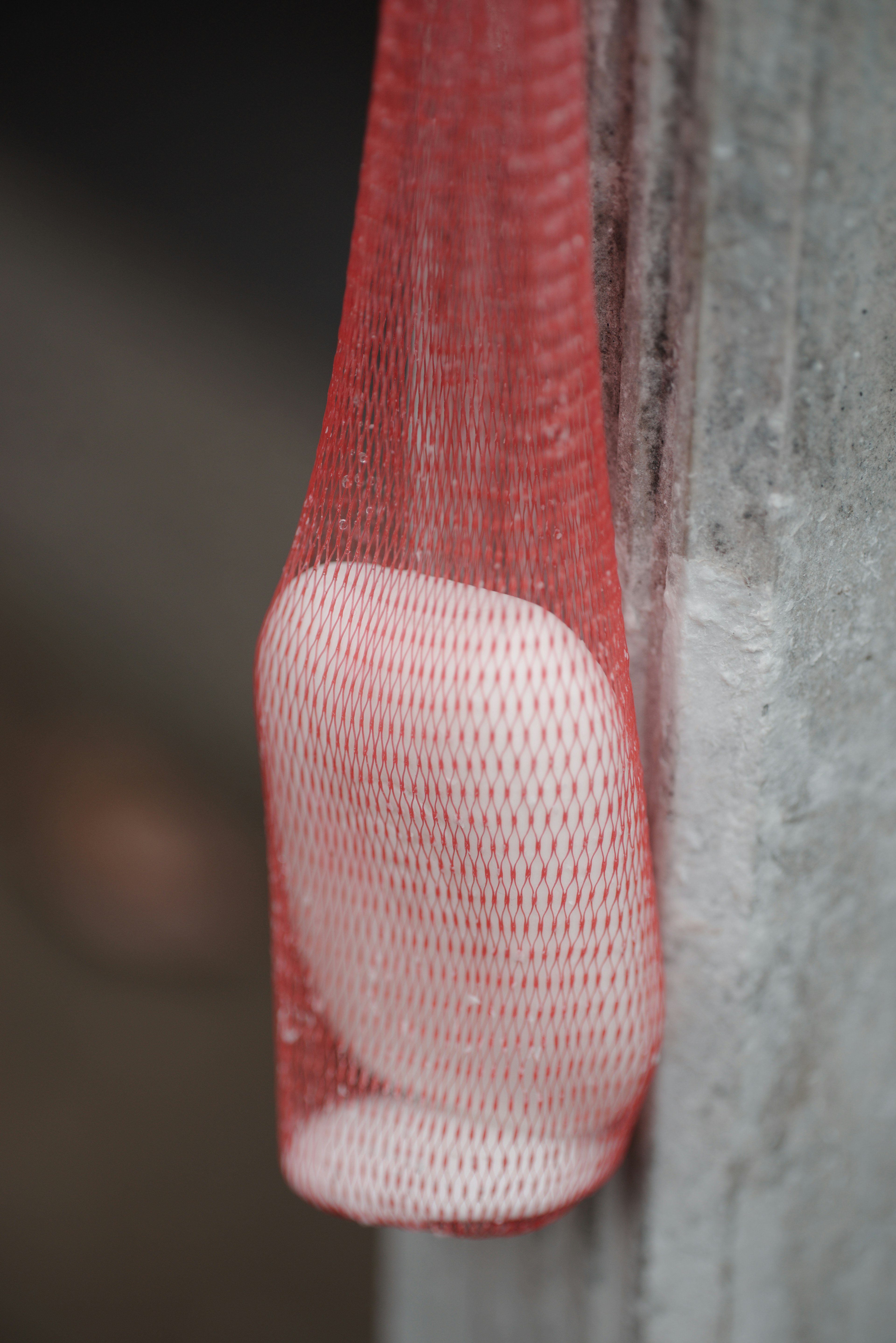 A white object hanging in a red net against a wall